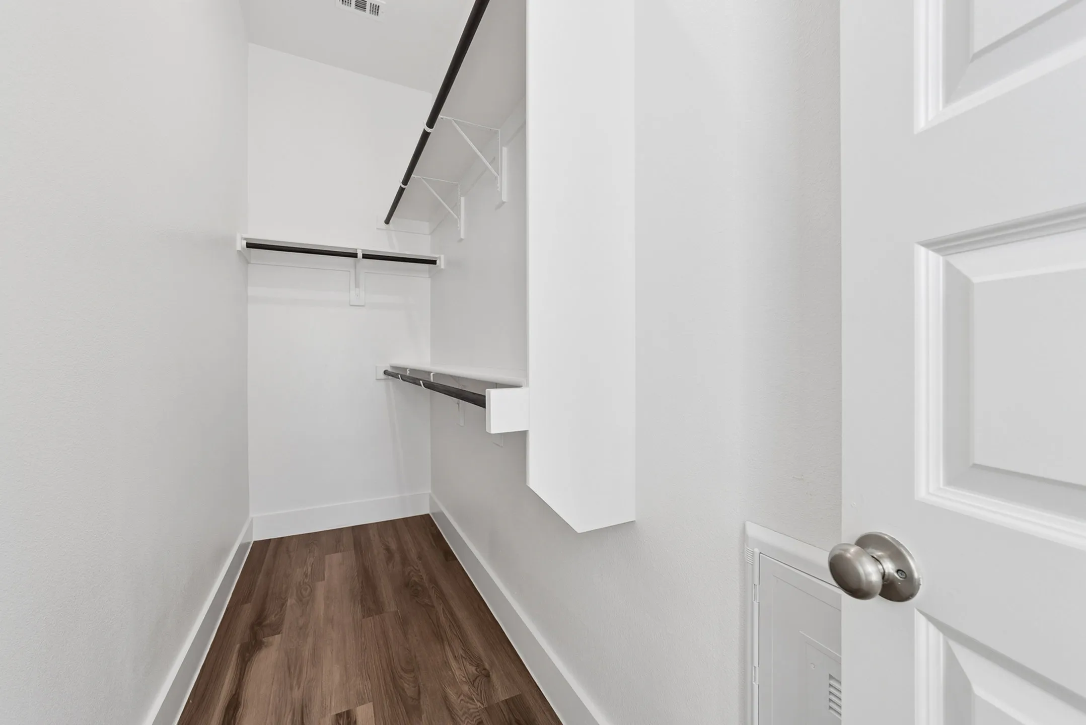 Spacious walk-in closet with sleek wooden flooring and ample hanging space.