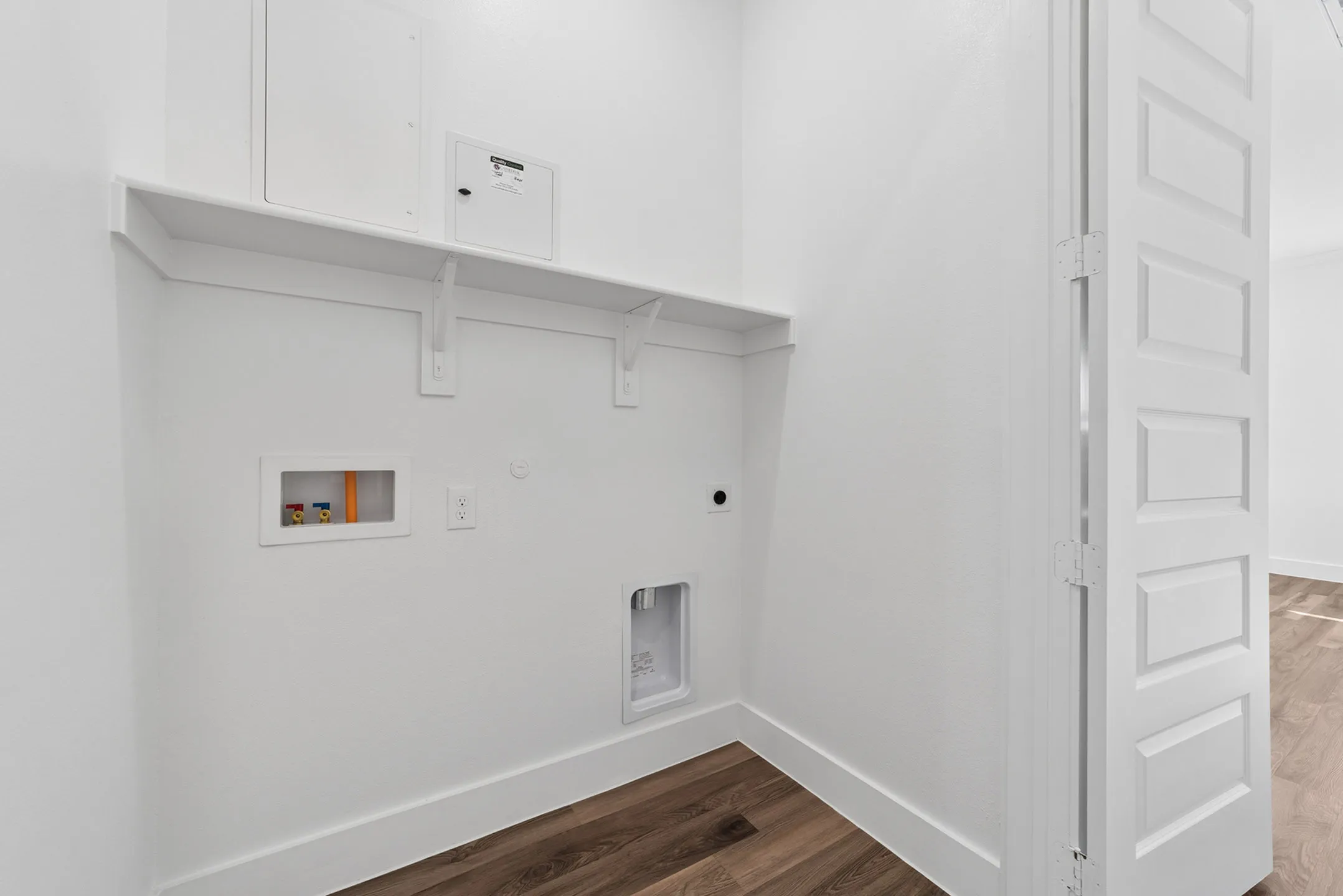 Chic modern laundry nook with clean white walls, a built-in shelf, and utility connections, perfect for efficient home living.