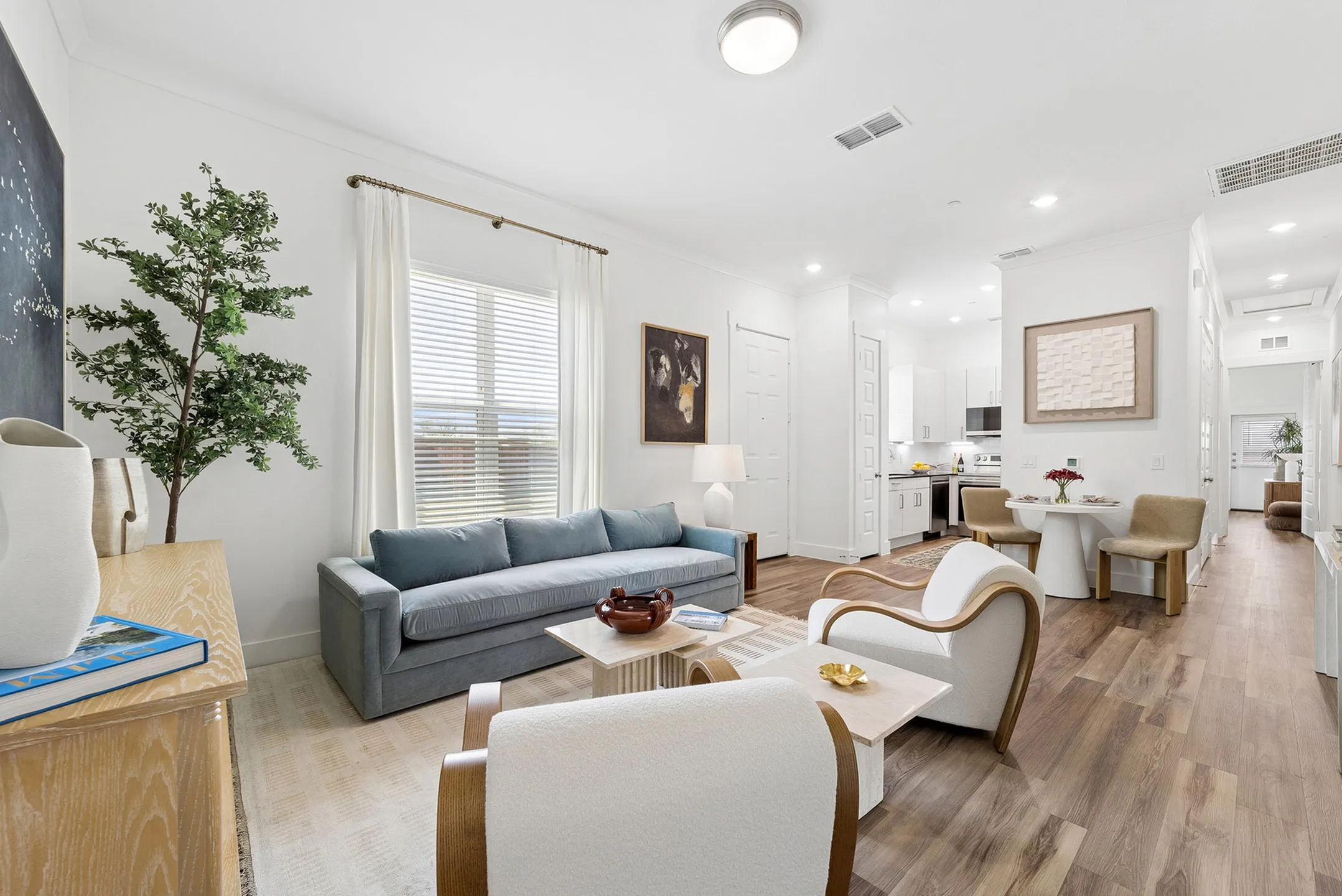 Bright and inviting living space featuring modern decor, a comfortable blue sofa, elegant armchairs, and an open kitchen with dining area.