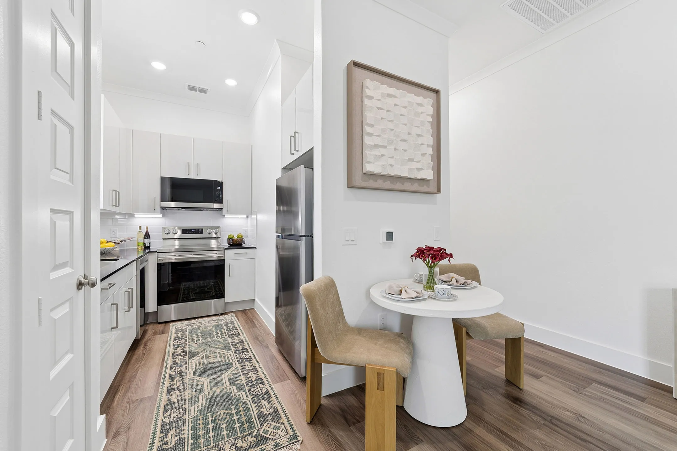 Modern apartment kitchen with sleek white cabinets, stainless steel appliances, and cozy dining nook with stylish chairs and decor.