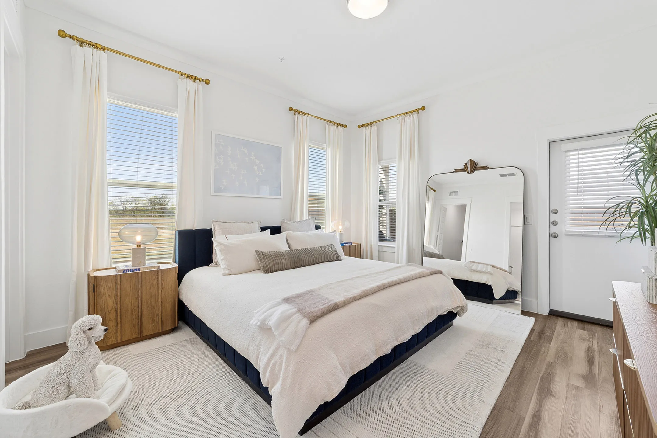 Bright and airy bedroom with large windows, elegant decor, and cozy bedding, featuring a stylish floor lamp and a plush carpet accent.