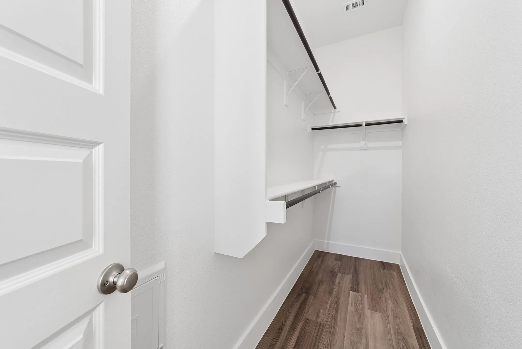 Elegant walk-in closet with sleek wooden flooring and ample hanging space, perfect for organized living.