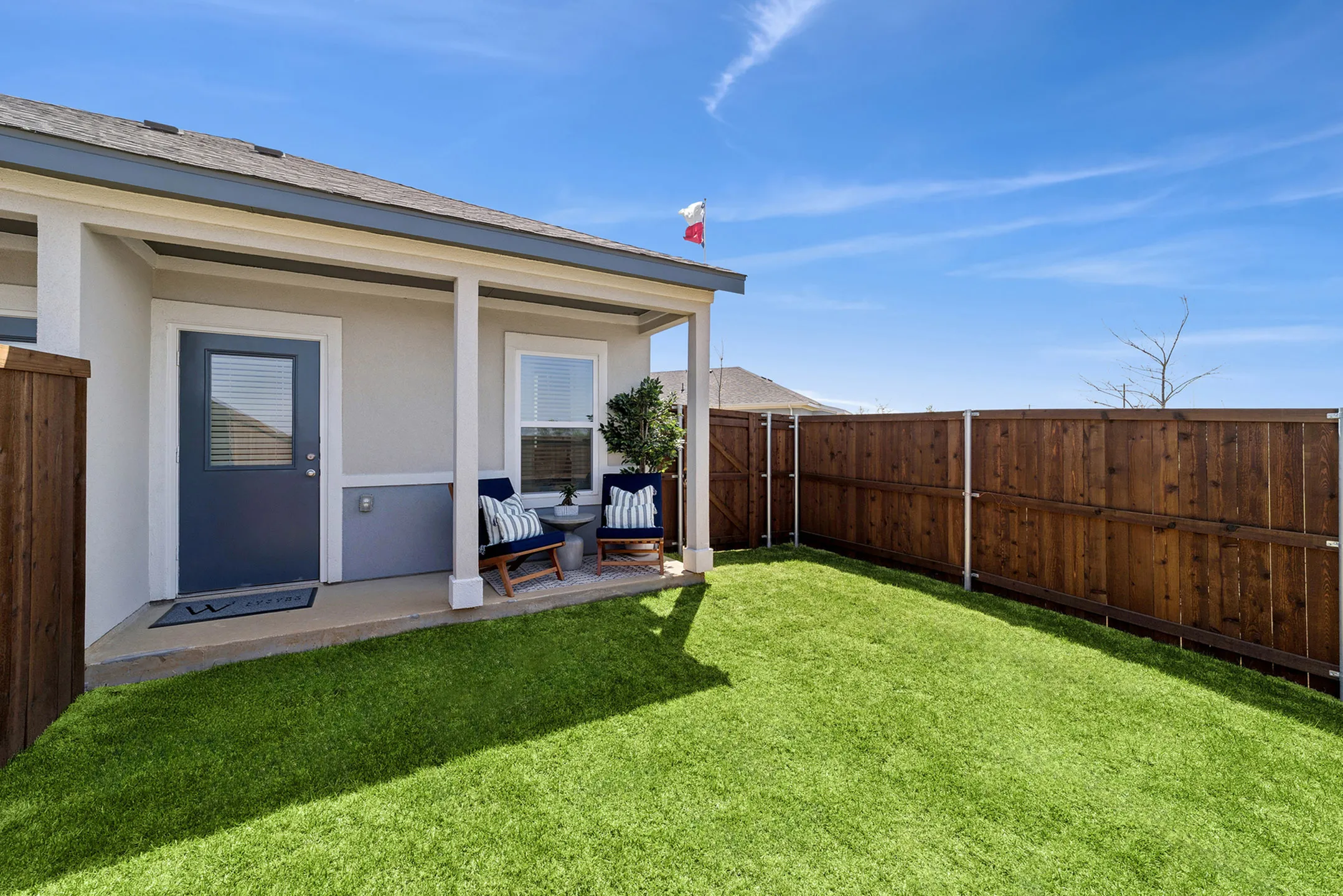 Charming backyard patio with cozy seating, vibrant green grass, and wooden privacy fence under a bright blue sky.