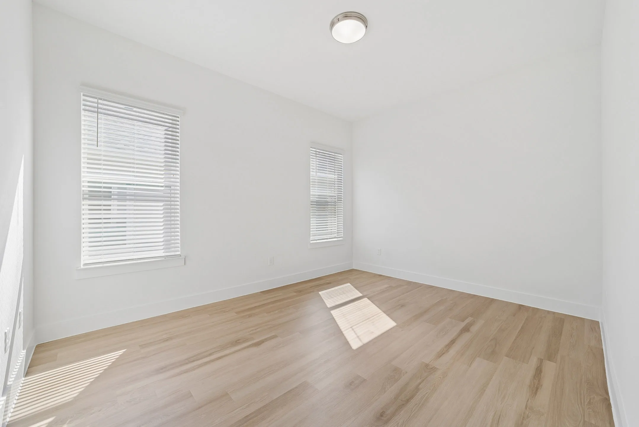 Bright and inviting empty room with large windows, showcasing elegant wooden flooring and abundant natural light.