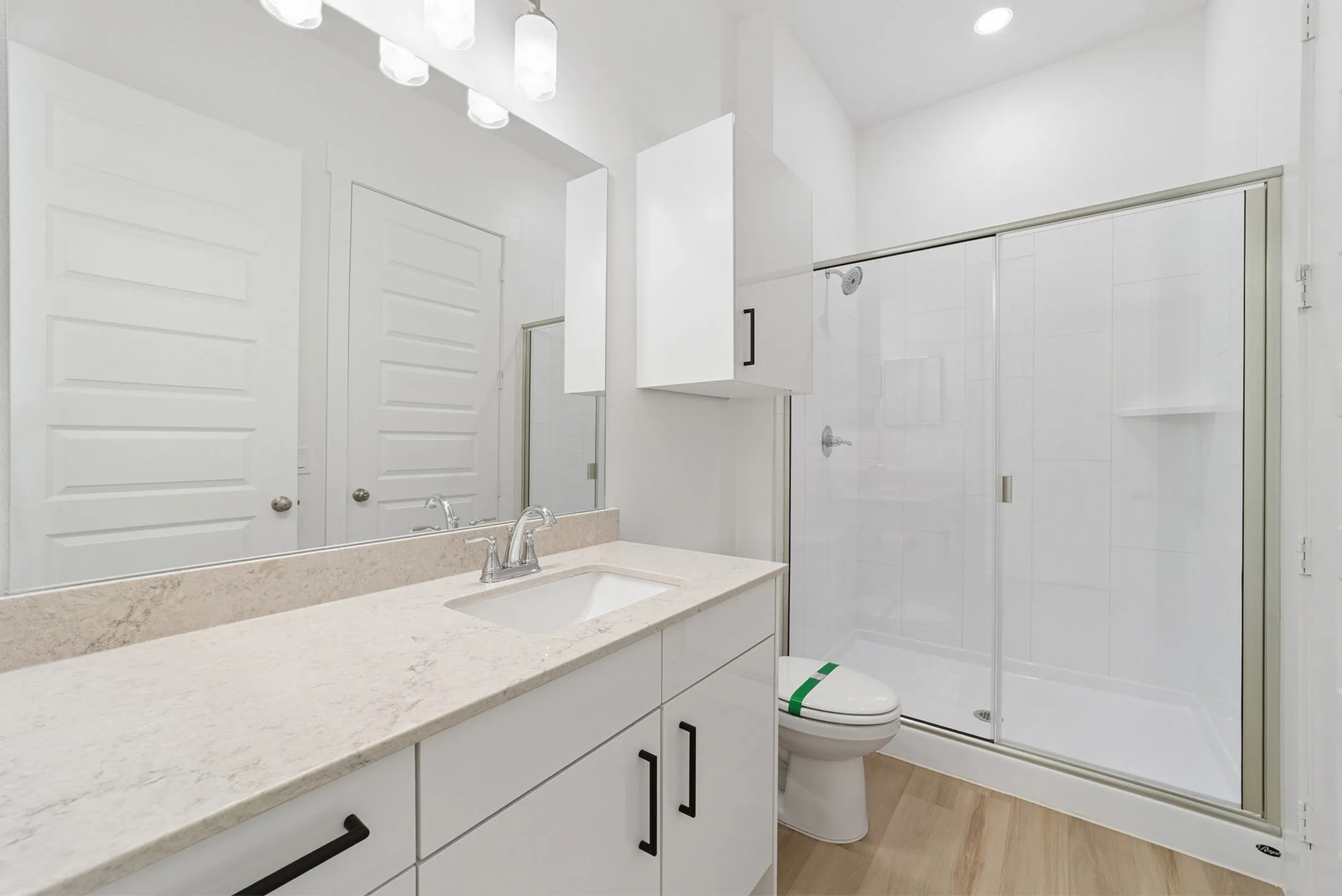 Modern bathroom with sleek white cabinetry, spacious countertop, and a glass-enclosed shower.