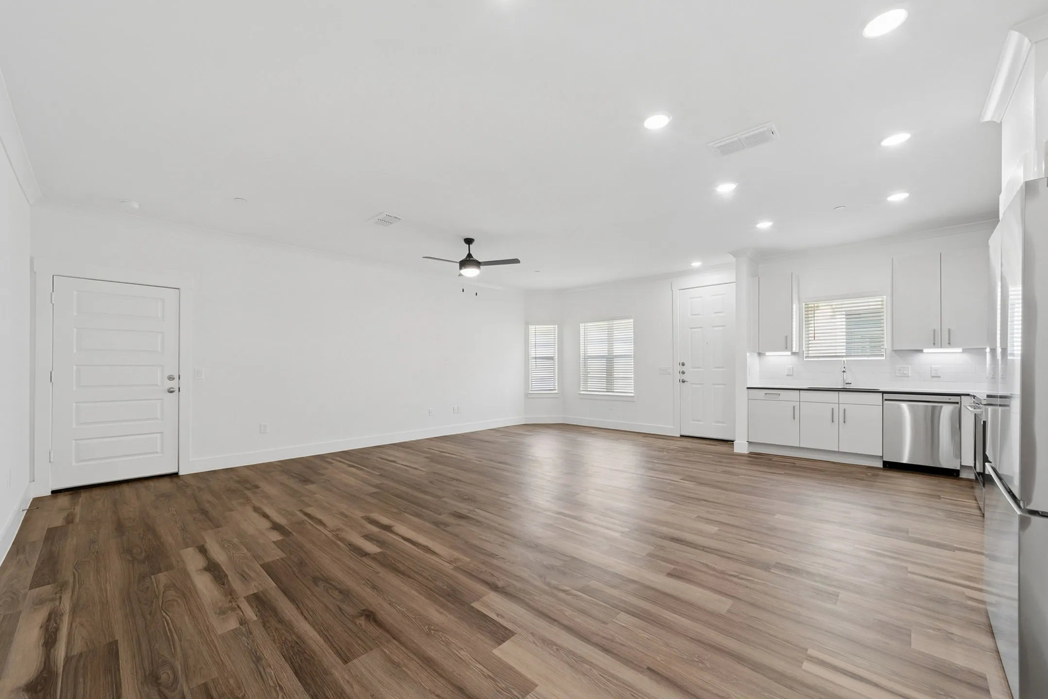 Open-concept living space featuring sleek hardwood floors, a modern kitchen with stainless steel appliances, and bright natural lighting.