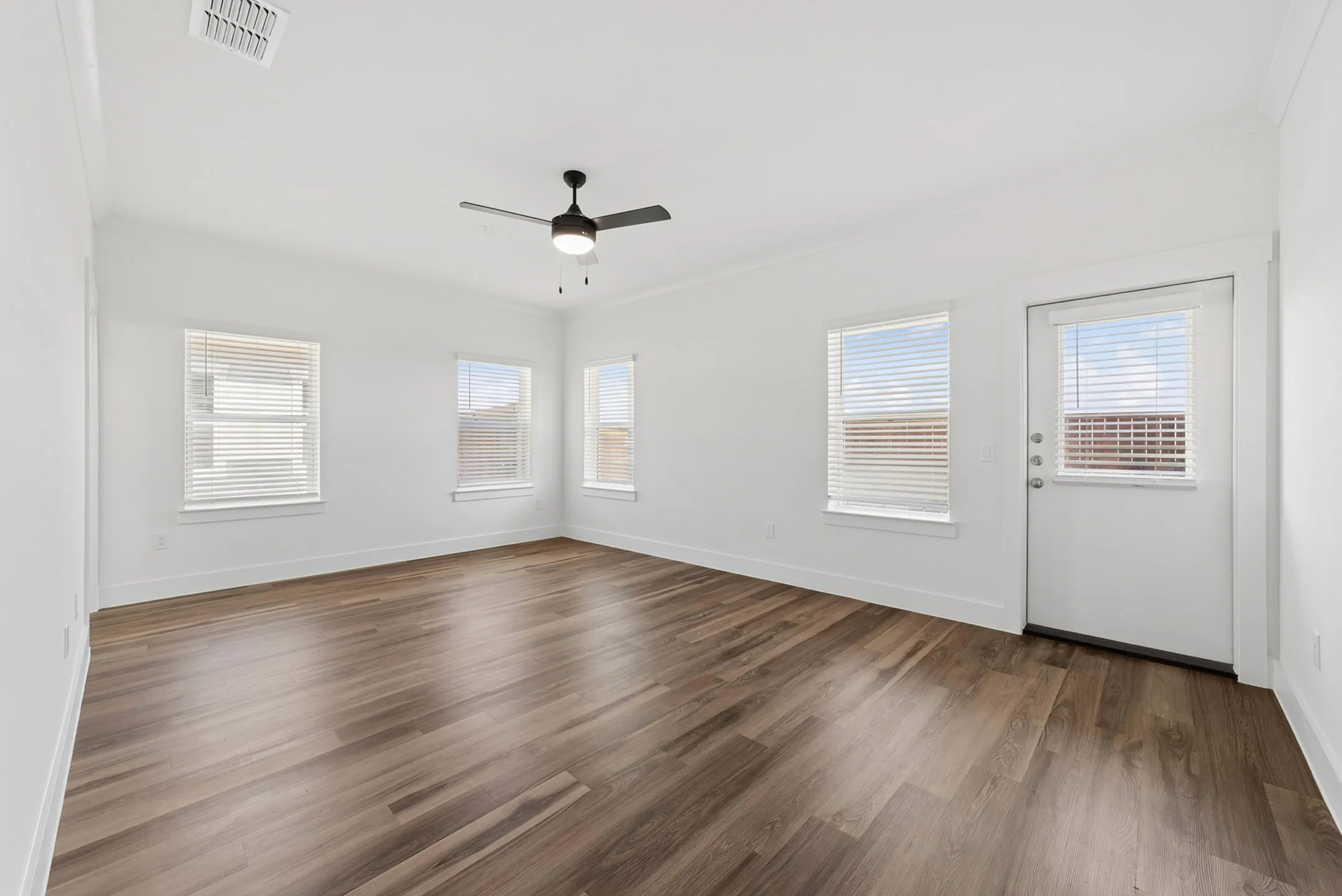 Bright, spacious room with elegant wood flooring, large windows, and a modern ceiling fan, perfect for versatile living arrangements.