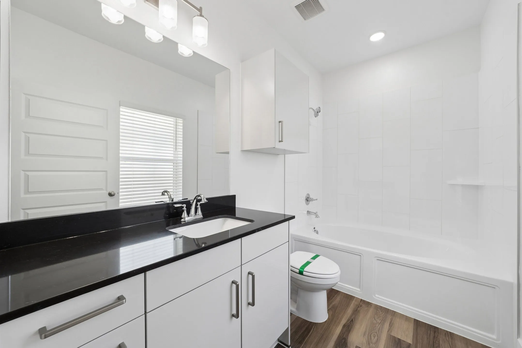 Sleek modern bathroom featuring a stylish black countertop, large mirror, and pristine white bathtub.