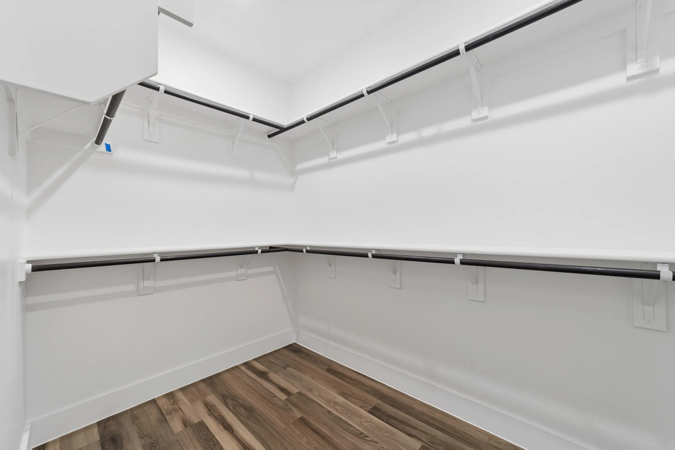 Spacious walk-in closet with sleek hanging rods, bright white walls, and elegant wood flooring, offering ample storage space.