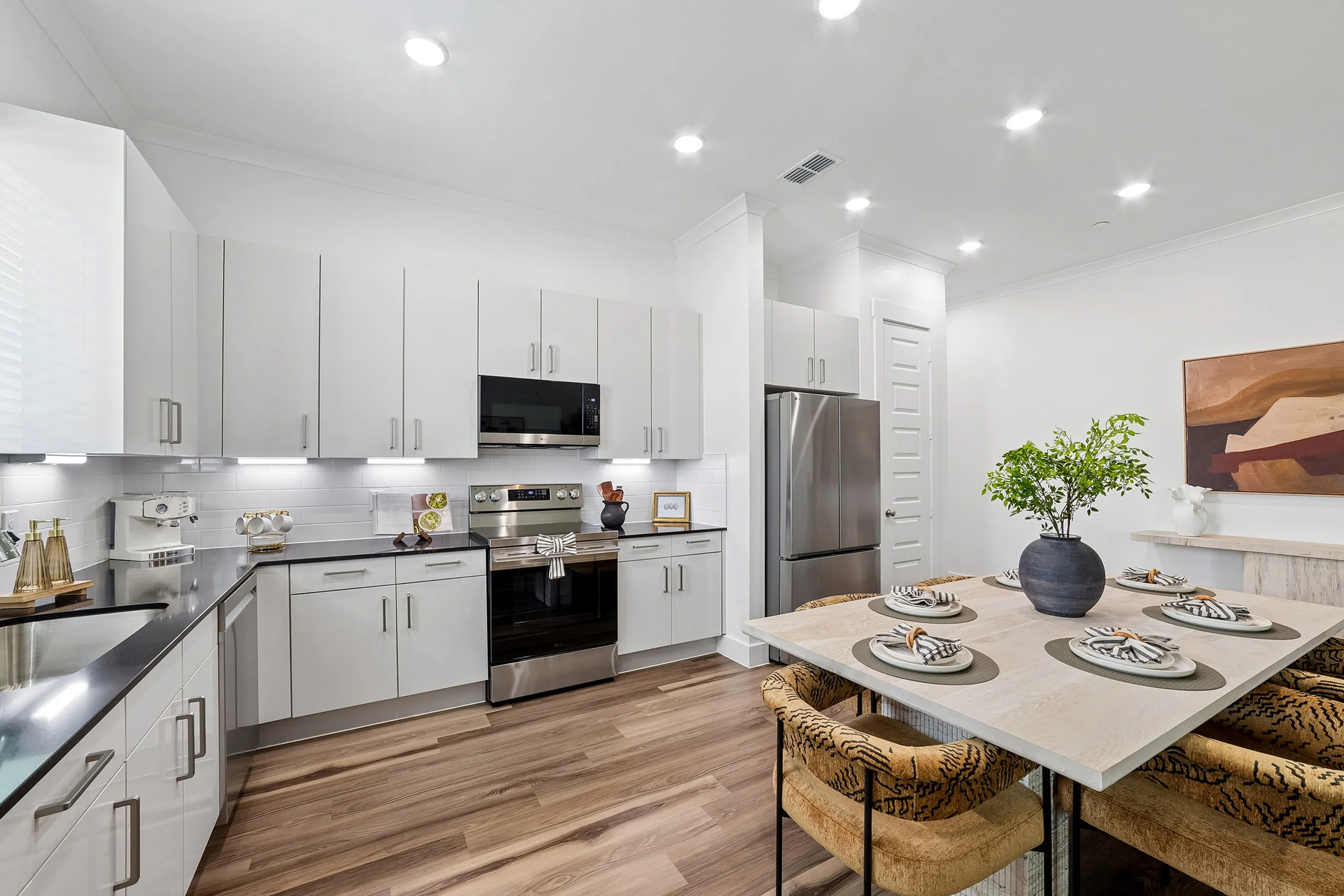 Modern kitchen with sleek white cabinetry, stainless steel appliances, and elegant dining table set for four.