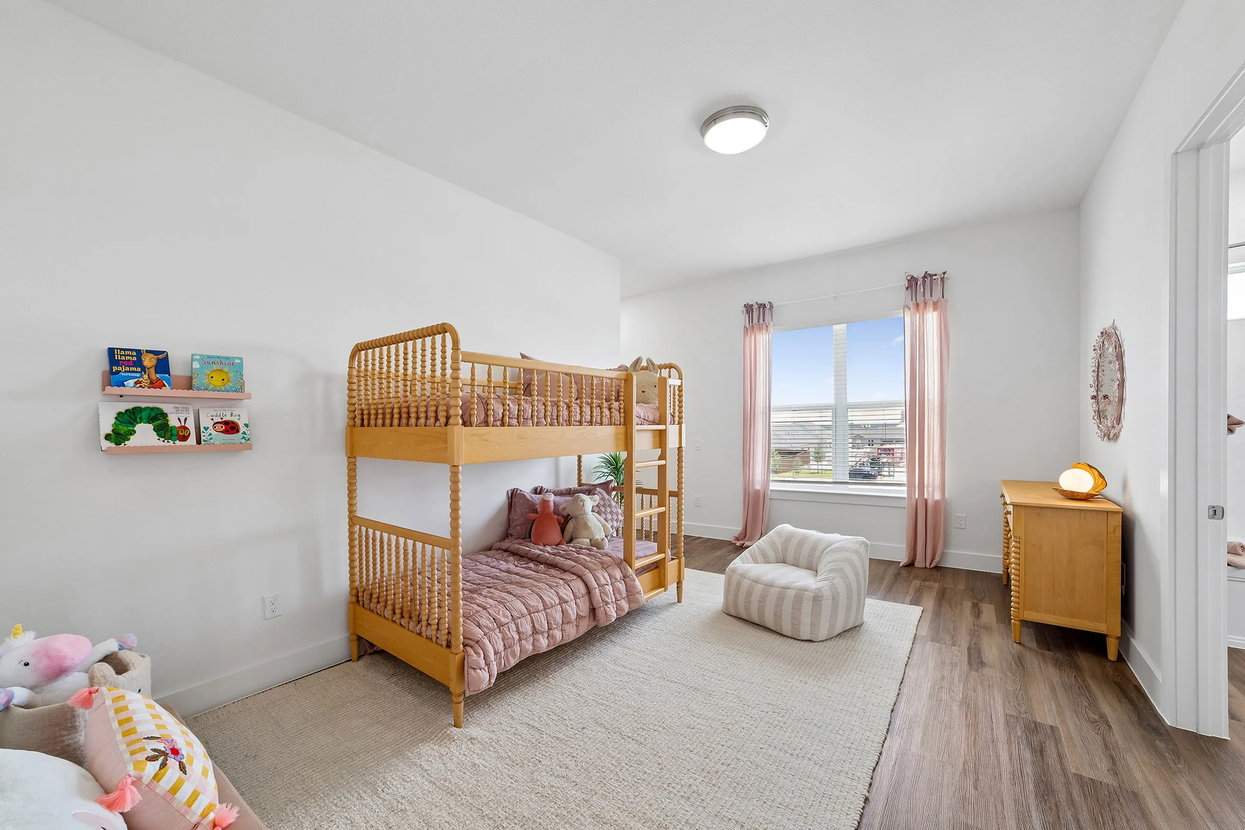 Bright and cozy children's bedroom featuring a stylish wooden bunk bed, playful decor, and a large window with pink curtains.