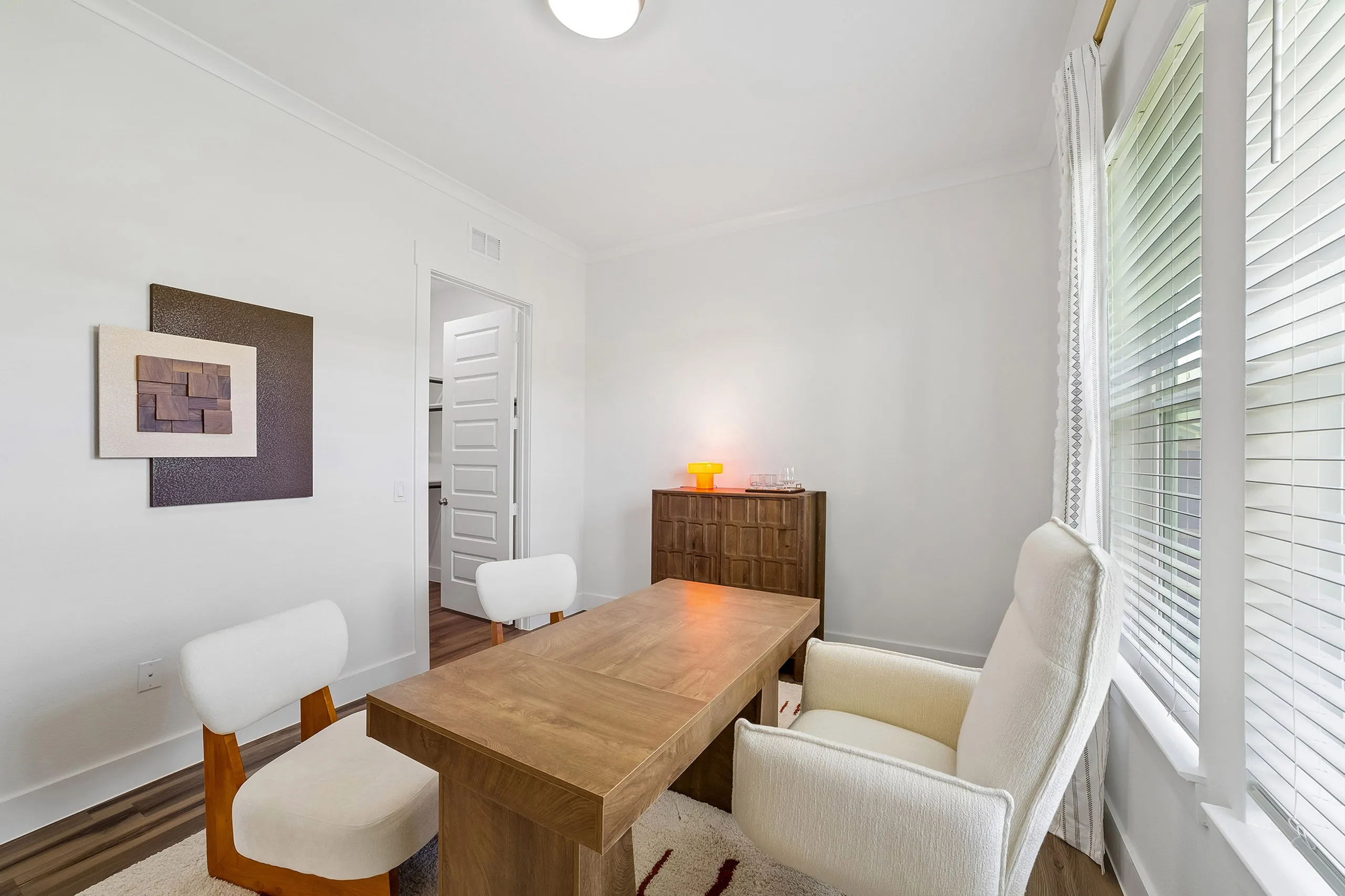 Inviting home office with natural light, modern wooden desk, and cozy white chairs.