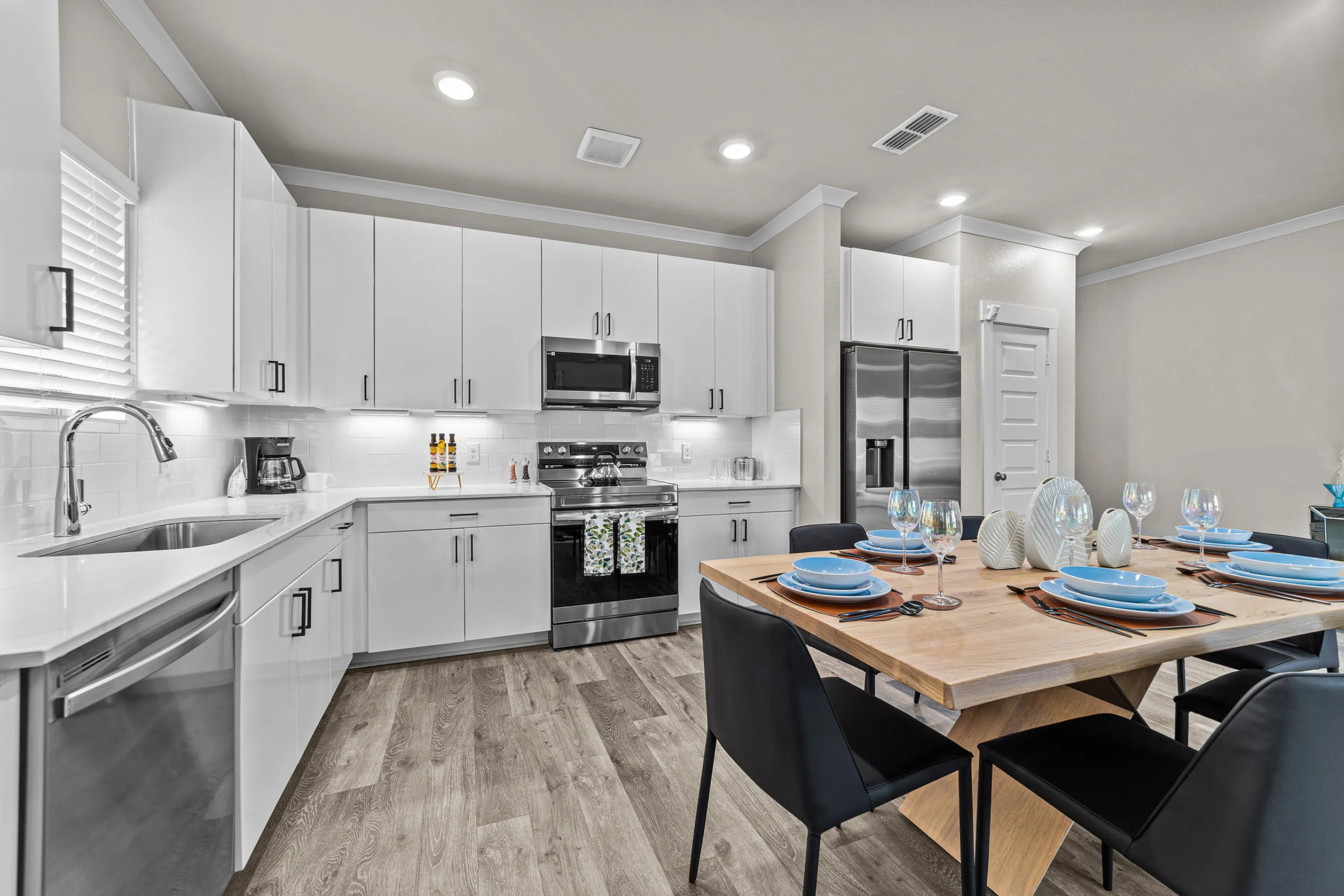 Modern kitchen with sleek white cabinets, stainless steel appliances, and a stylish dining area set for four.