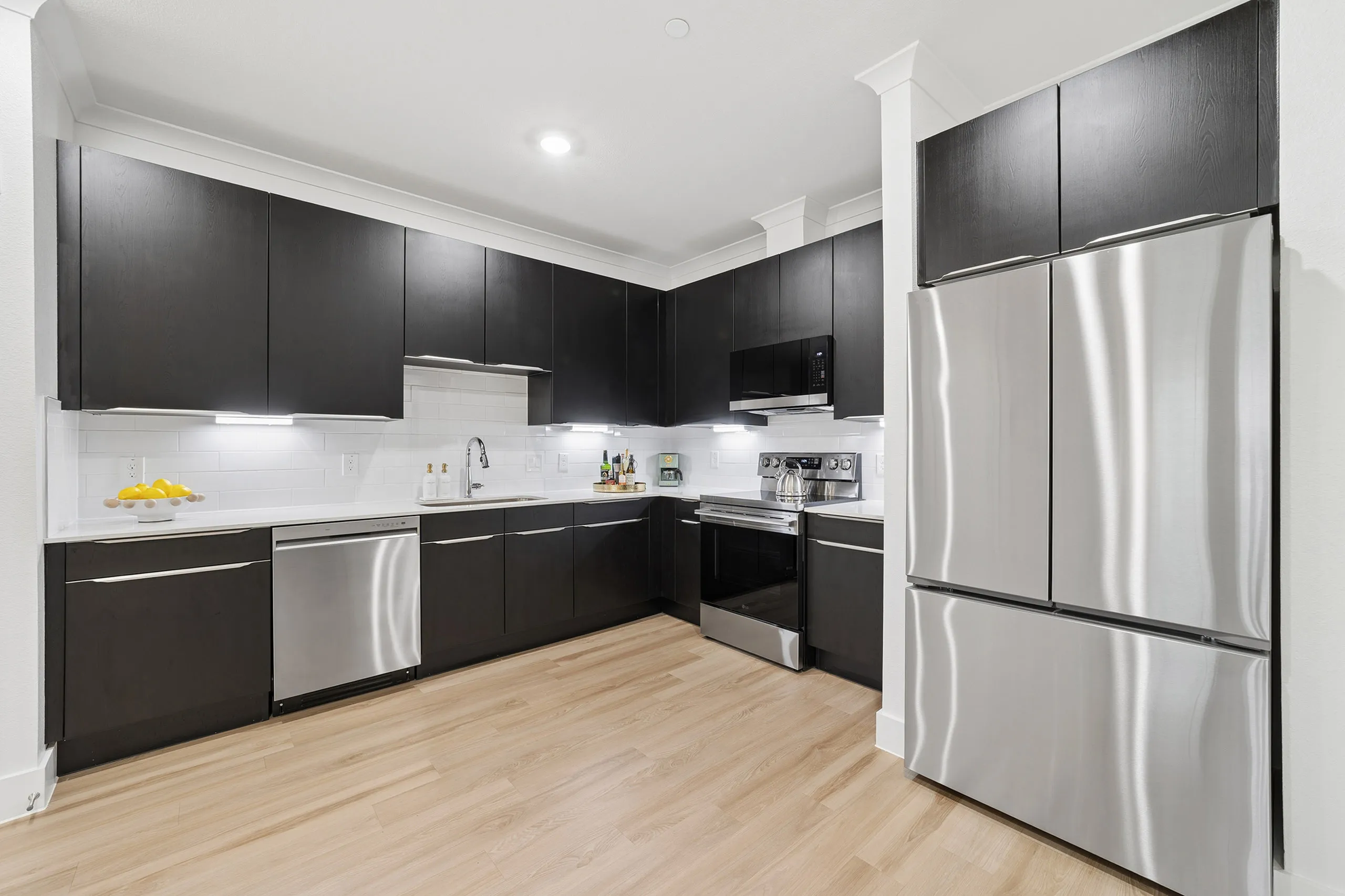 Modern kitchen with sleek black cabinetry, stainless steel appliances, and elegant wood flooring.