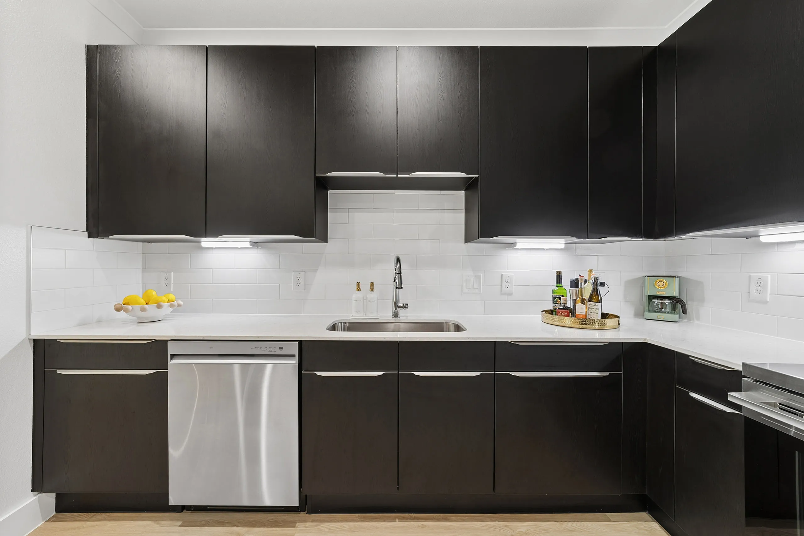 Sleek modern kitchen featuring dark cabinetry, stainless steel appliances, and a minimalist design with bright lighting and stylish decor.
