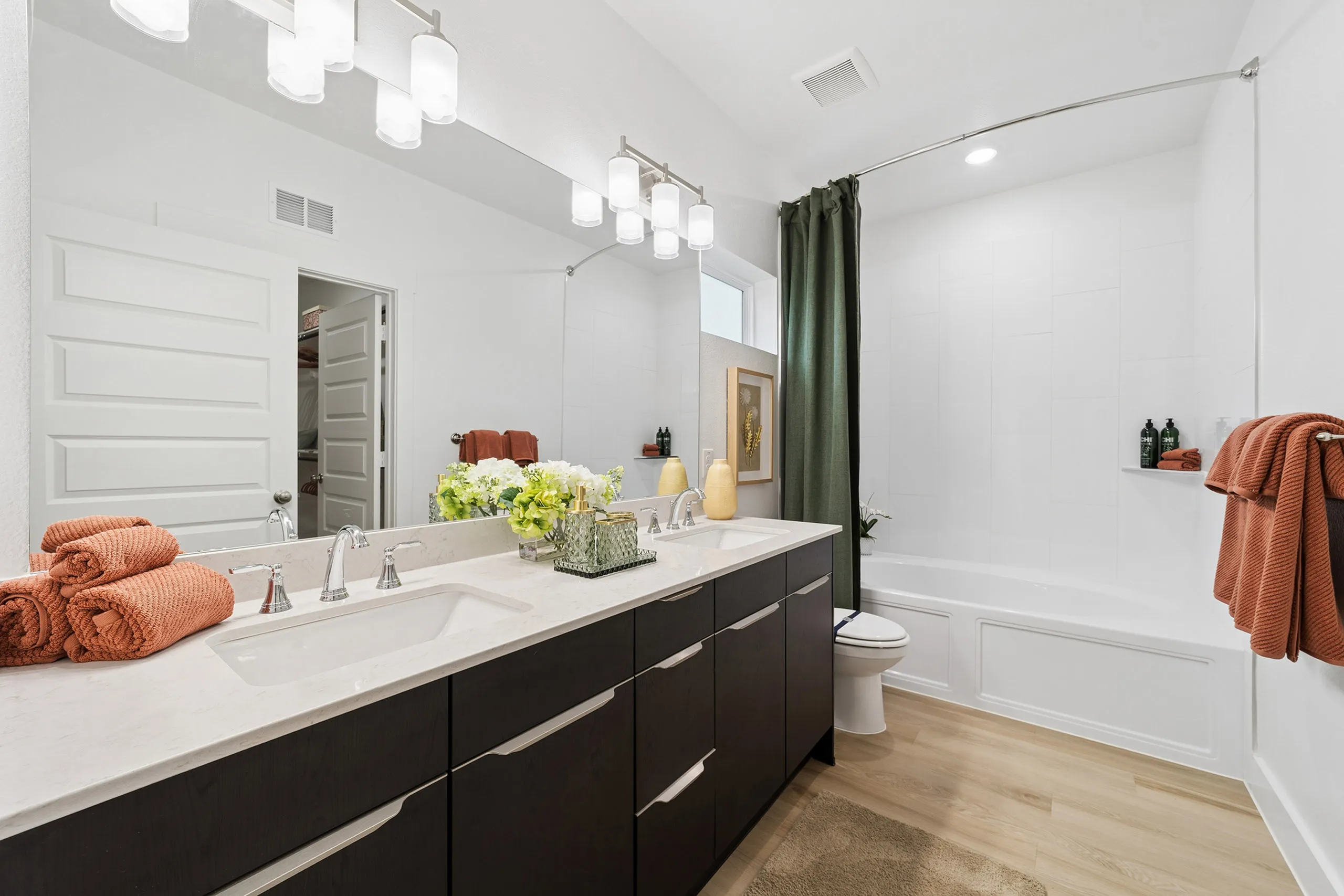 Elegant bathroom with dual sinks, modern lighting, and fresh decor, featuring a sleek bathtub and soft towels.