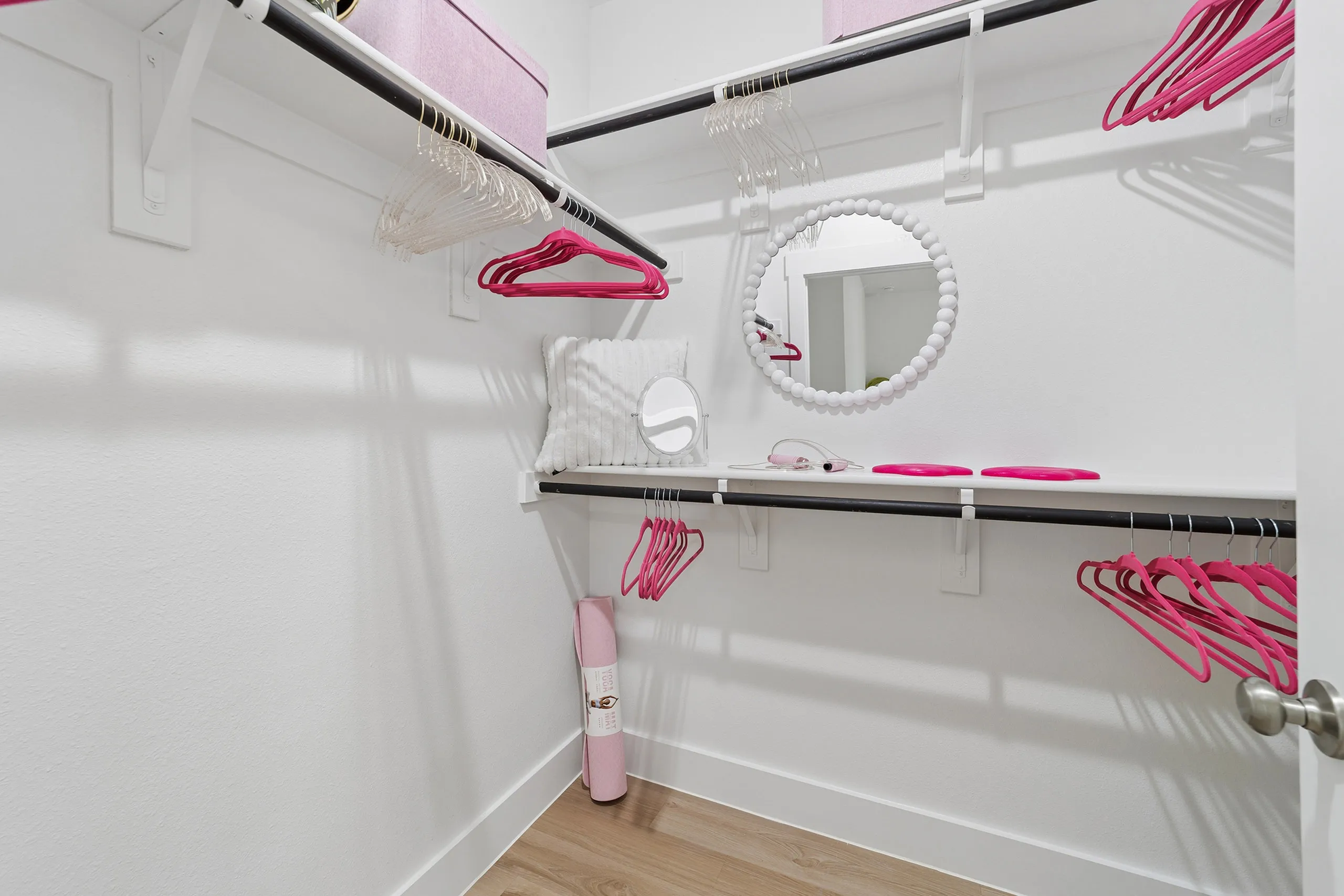 Chic walk-in closet with modern shelving, pink accents, and decorative mirror for a stylish storage solution.