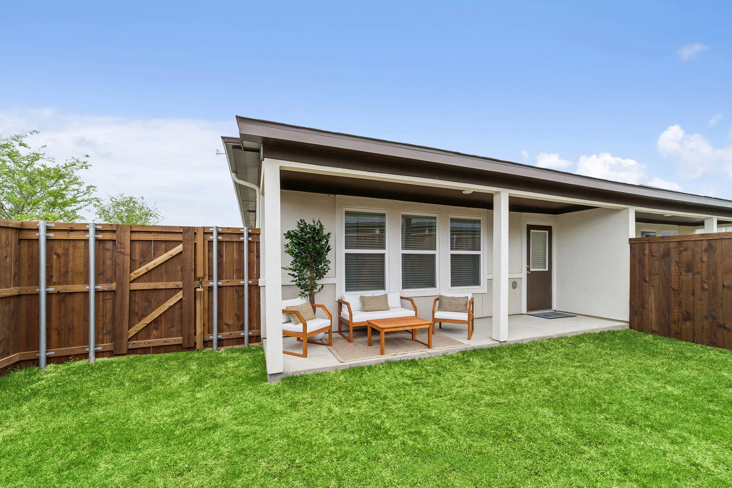 Charming outdoor patio with cozy seating area, surrounded by a wooden fence and lush green grass, perfect for relaxing and entertaining.