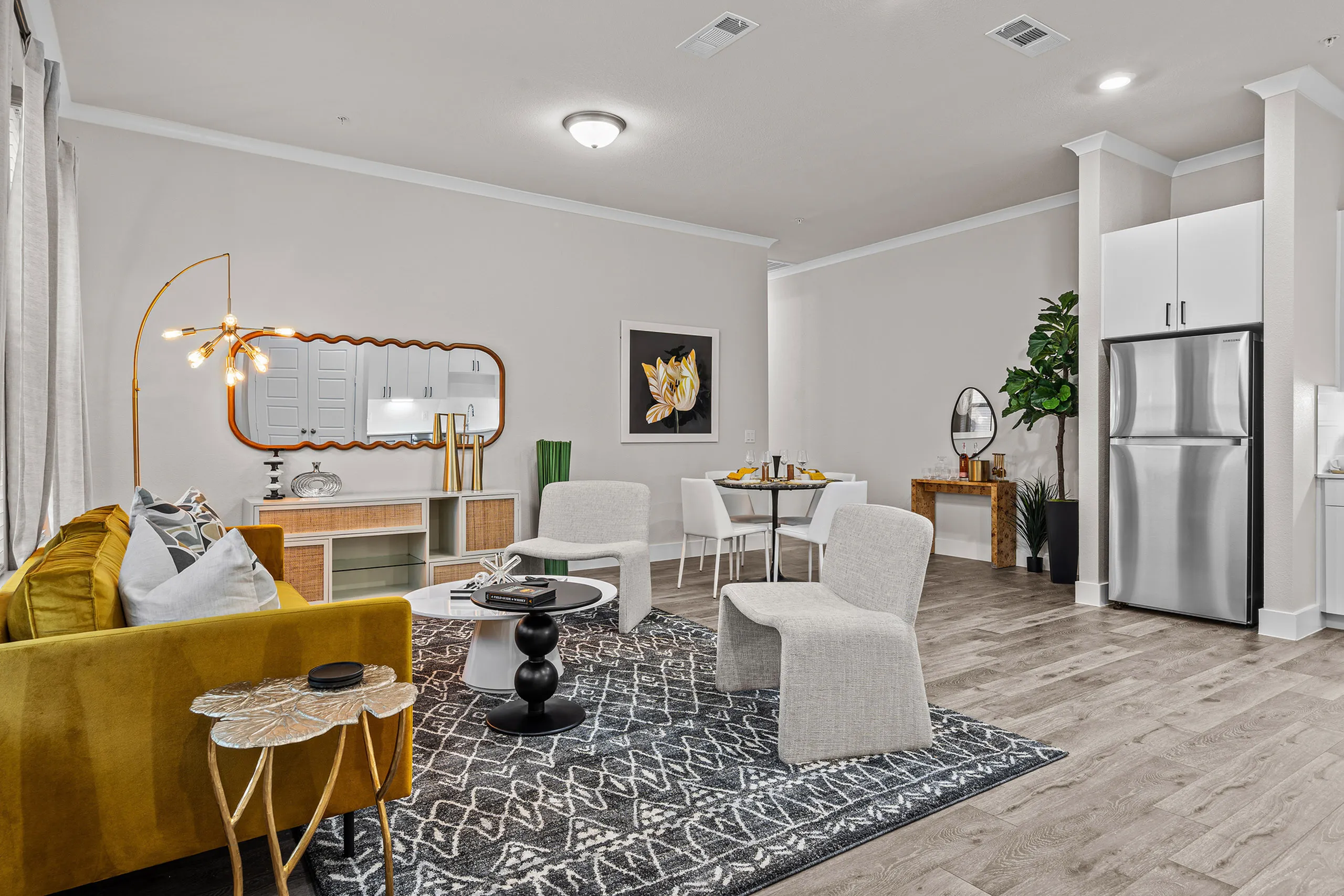 Modern open-concept living space with stylish decor, including a mustard velvet sofa, chic lighting, and a sleek stainless steel refrigerator.