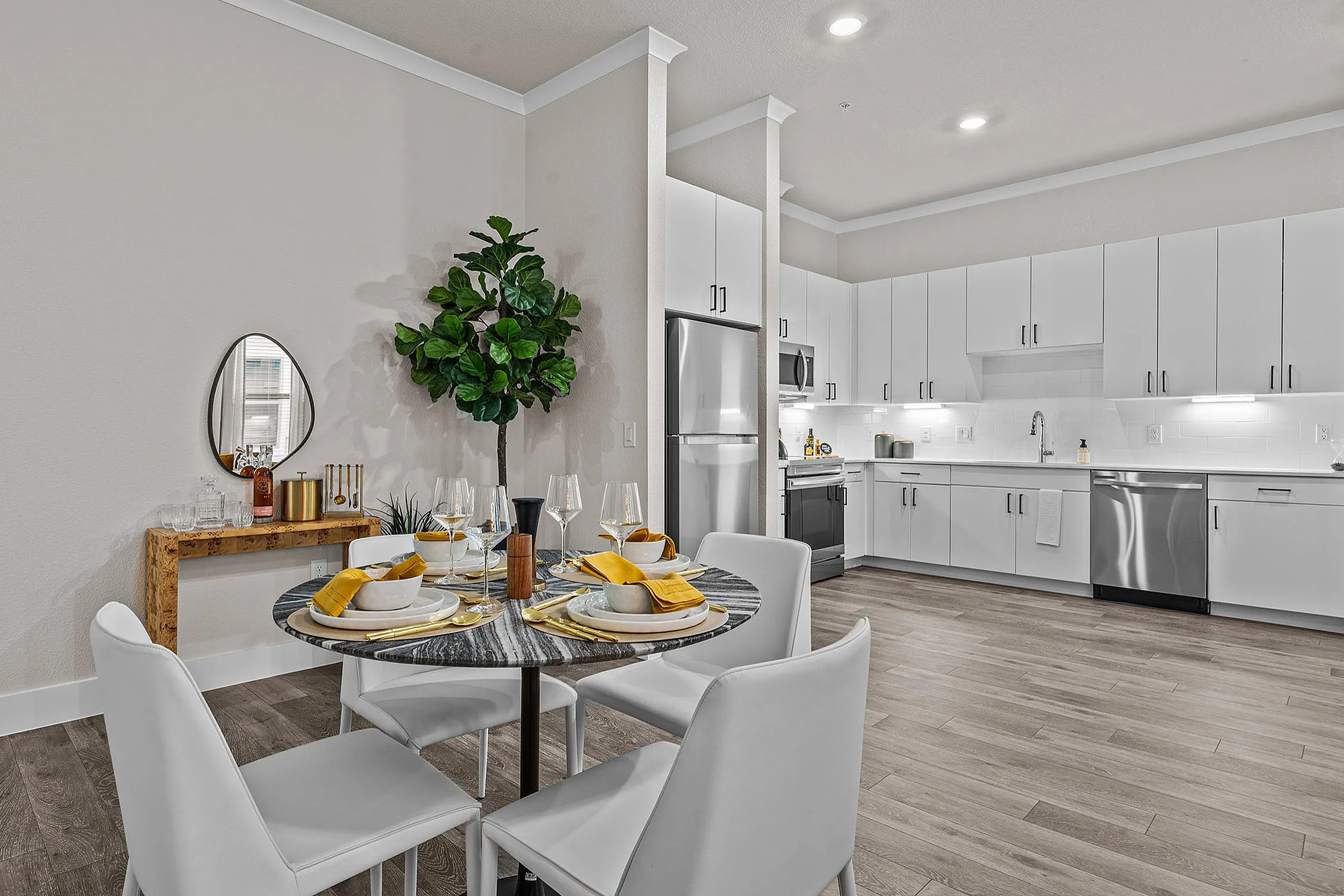 Contemporary open-plan kitchen and dining area with sleek white cabinetry, stainless steel appliances, and a stylish round dining table set for four.