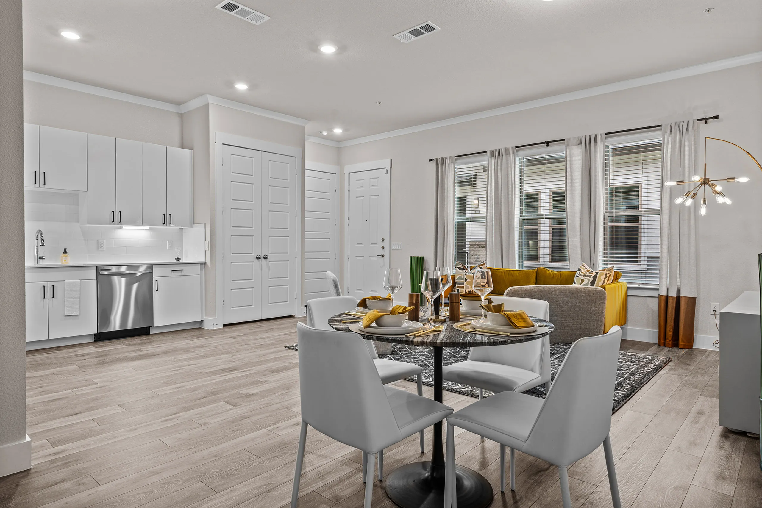 Modern open-concept living space featuring sleek kitchen cabinetry, elegant dining area, and cozy seating with large windows.