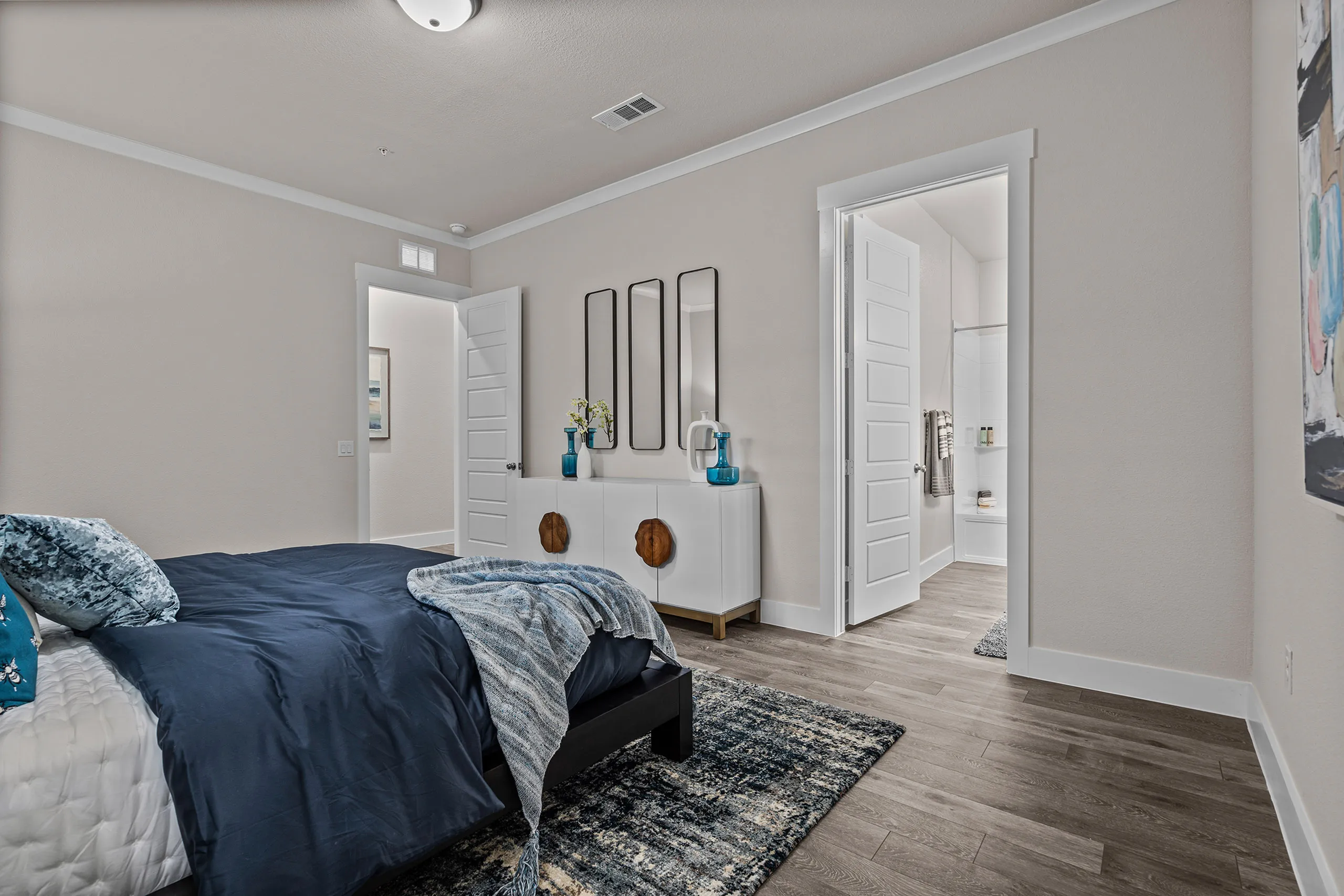 Chic bedroom with elegant decor, featuring a cozy bed with blue accents and access to a modern bathroom.