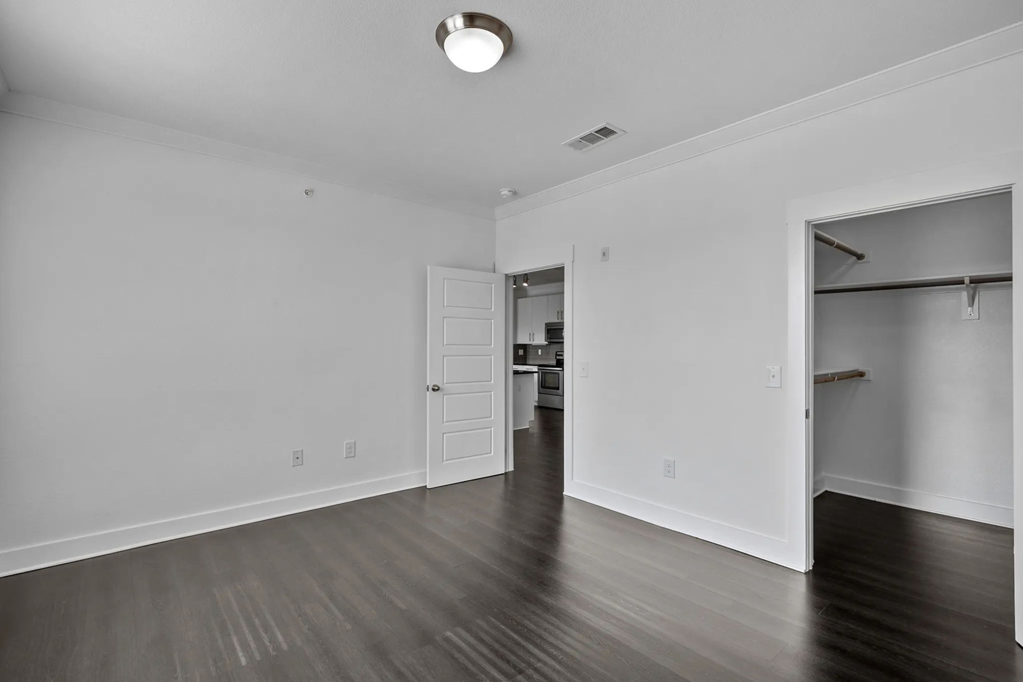 Bright, modern bedroom with hardwood floors, spacious walk-in closet, and direct access to a sleek kitchen.