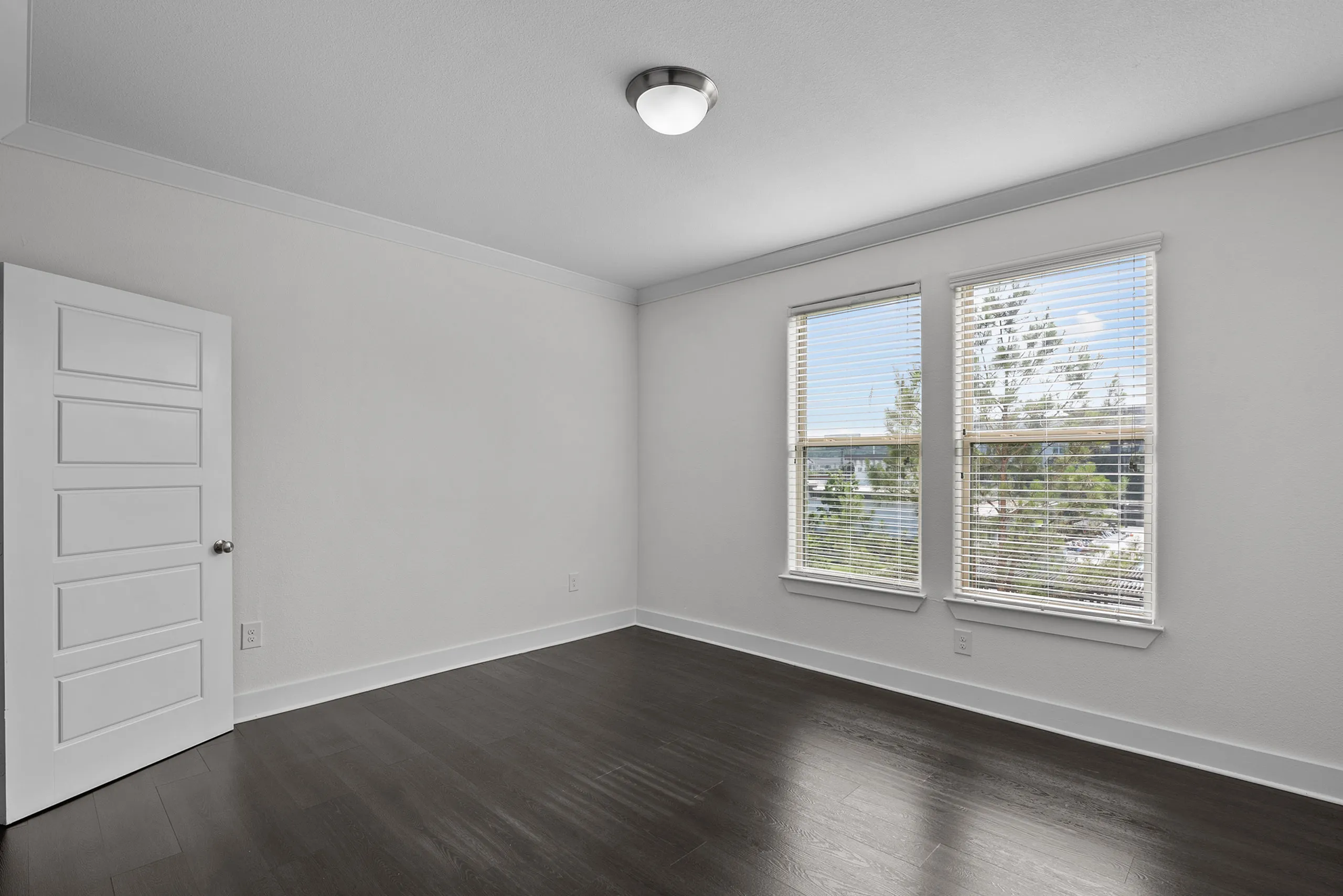 Bright and modern room with dark wood flooring and large windows showcasing natural light.