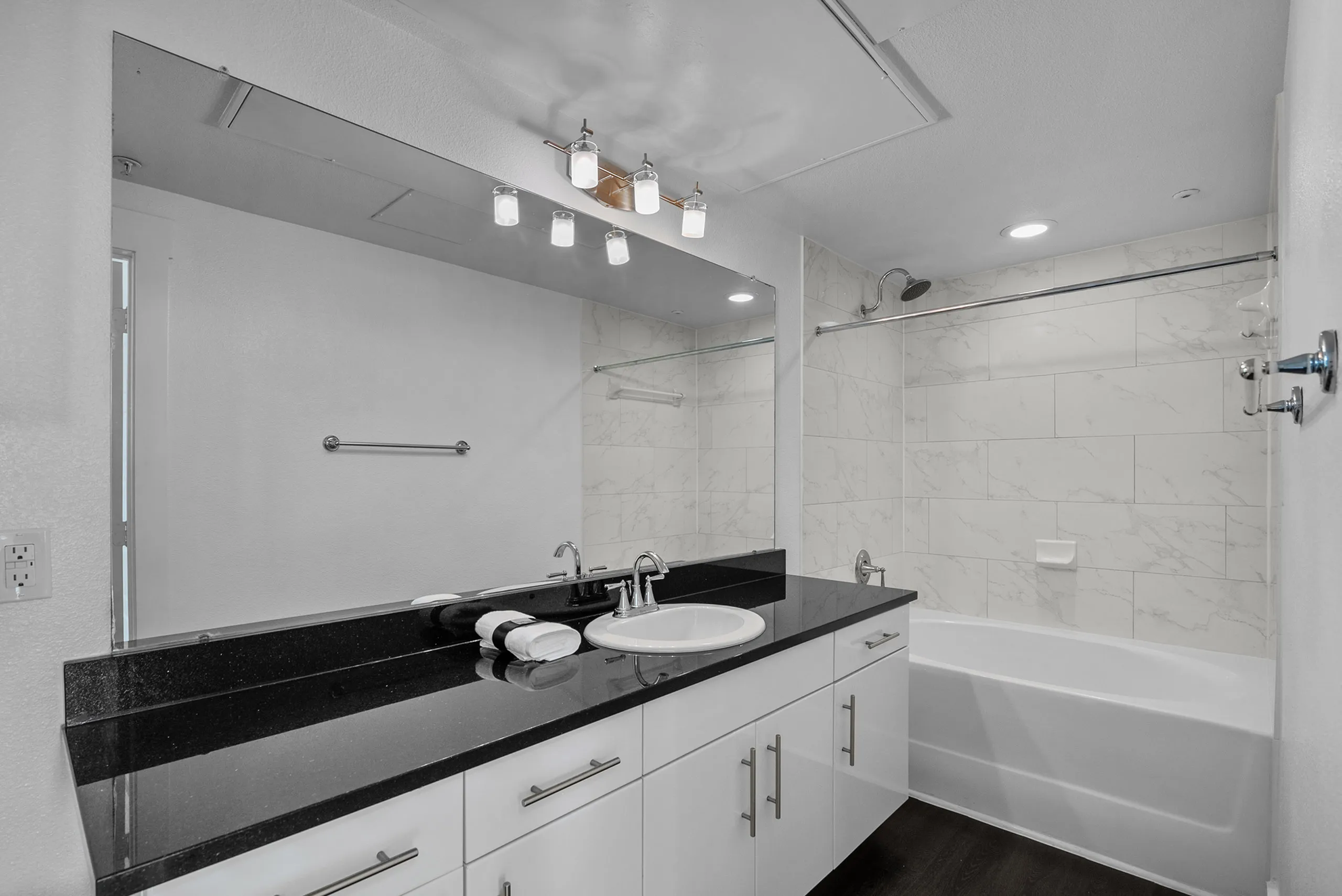 Modern bathroom with sleek black countertop, white cabinetry, and a tile-surround bathtub under elegant lighting.