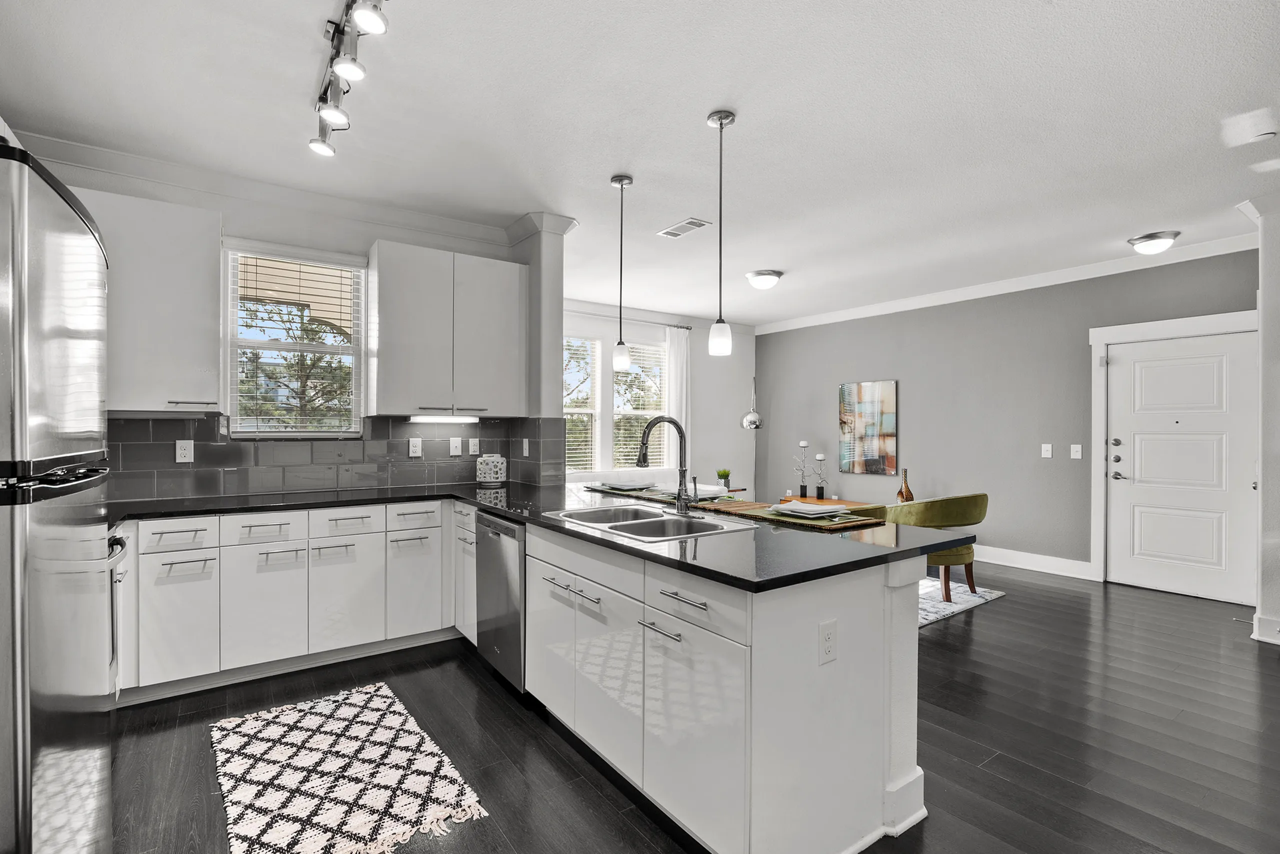 Modern kitchen with sleek white cabinetry, stainless steel appliances, and granite countertops, opening to a bright dining area.