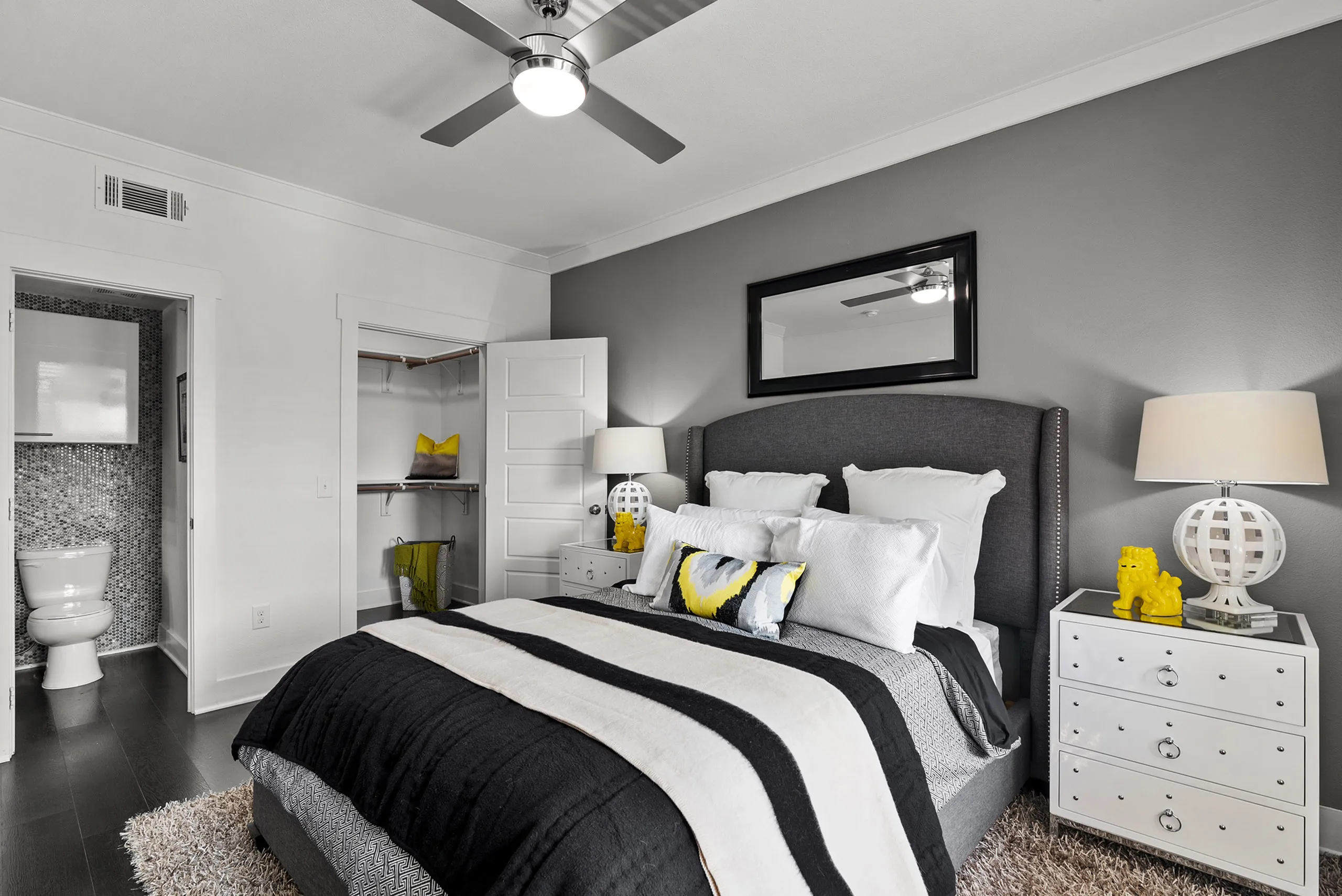 Elegant bedroom with modern decor featuring a cozy bed with striped bedding, stylish lamps, and an open closet adjacent to a chic bathroom.