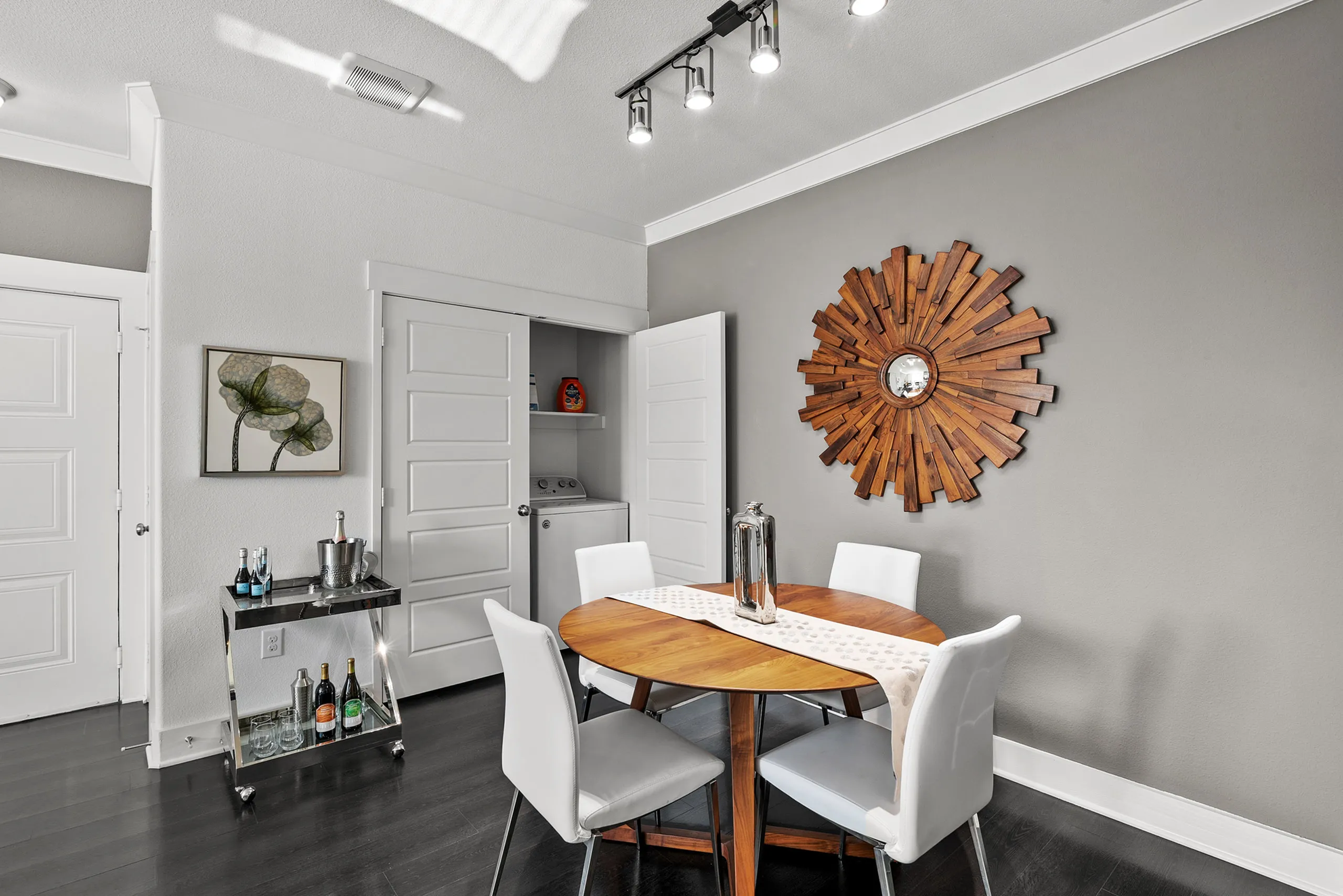 Chic dining area with modern round wooden table, elegant white chairs, and striking wall art, complemented by sleek bar cart and laundry nook.