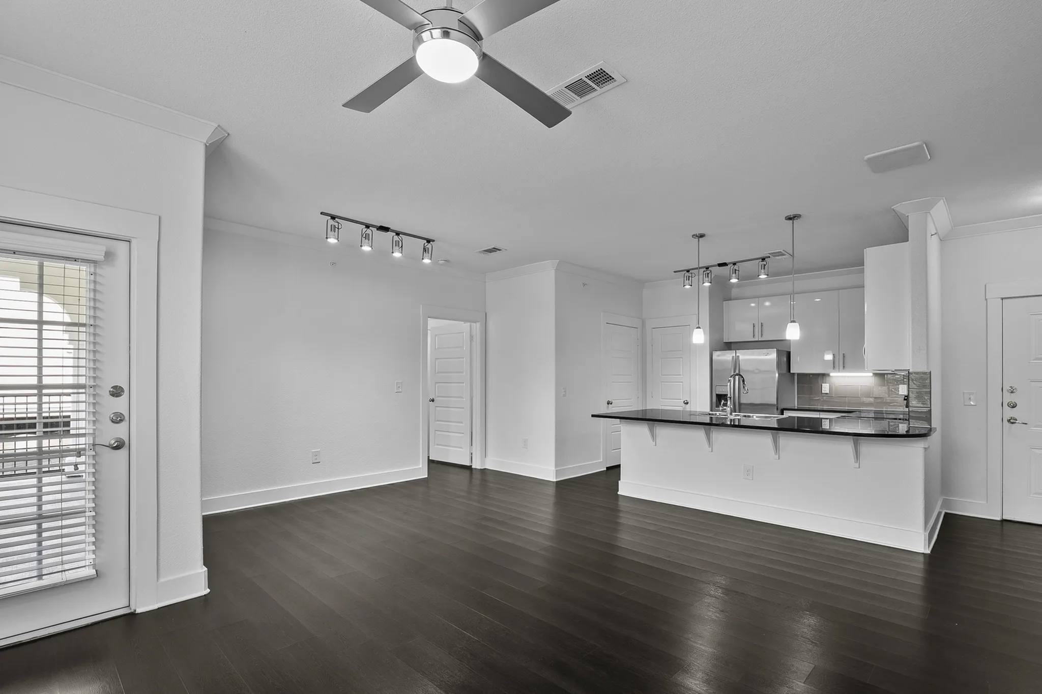 Modern open-concept living area with sleek dark flooring, stylish ceiling fan, and a contemporary kitchen featuring a chic breakfast bar and stainless steel appliances.