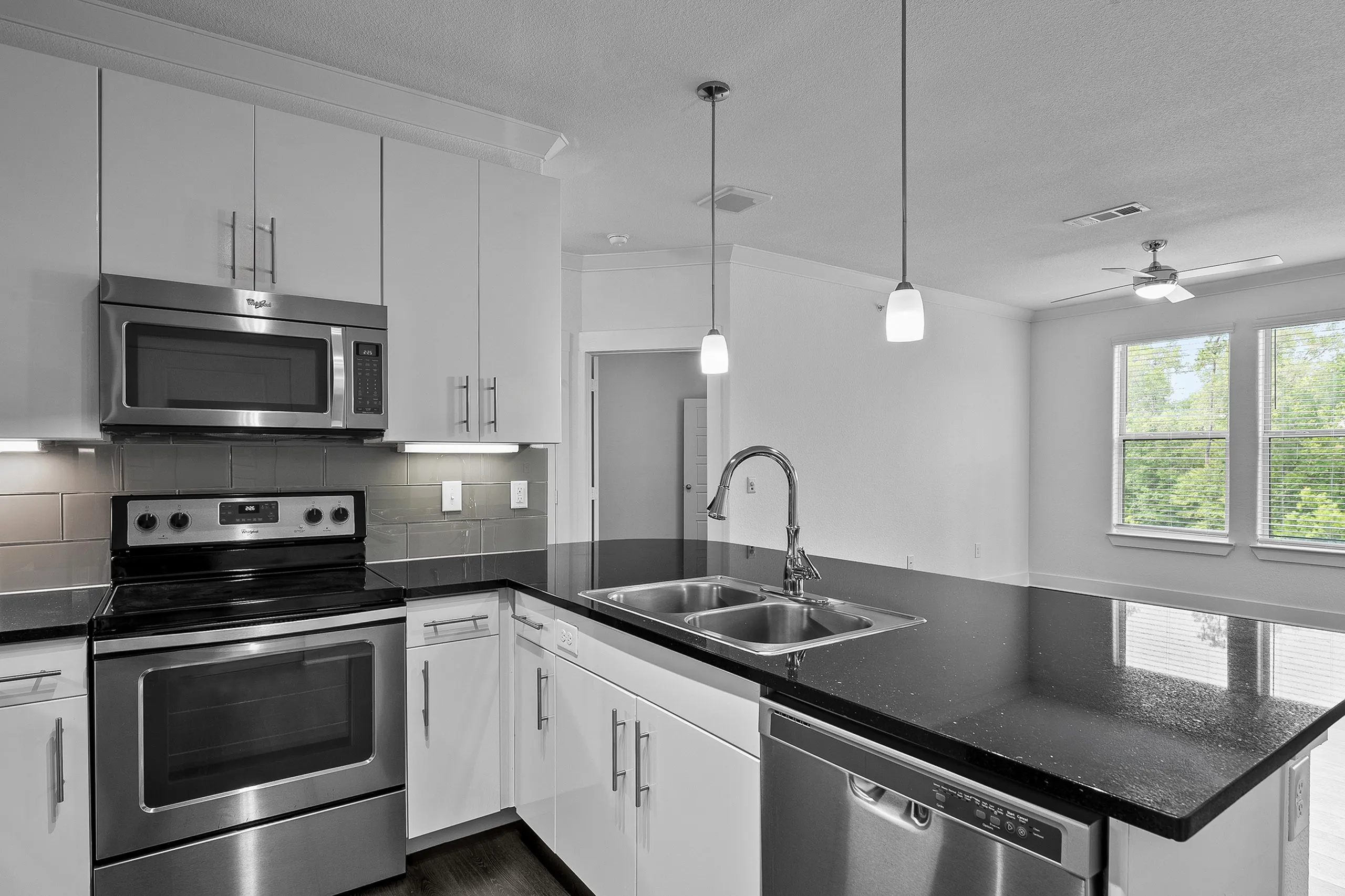 Modern kitchen with sleek stainless steel appliances, elegant black countertops, and ambient pendant lighting.