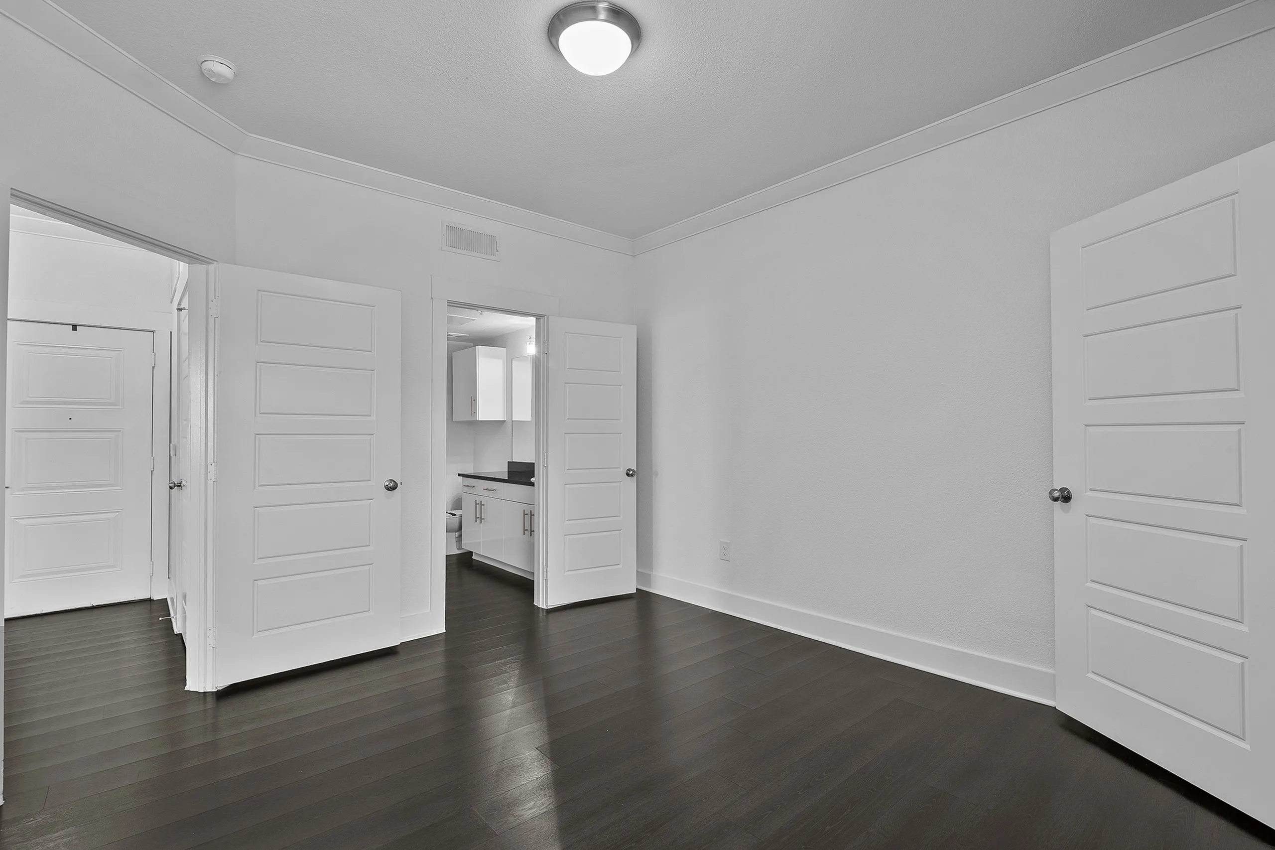 Bright and spacious room with elegant dark hardwood flooring, featuring modern white doors leading to a stylish kitchen area.