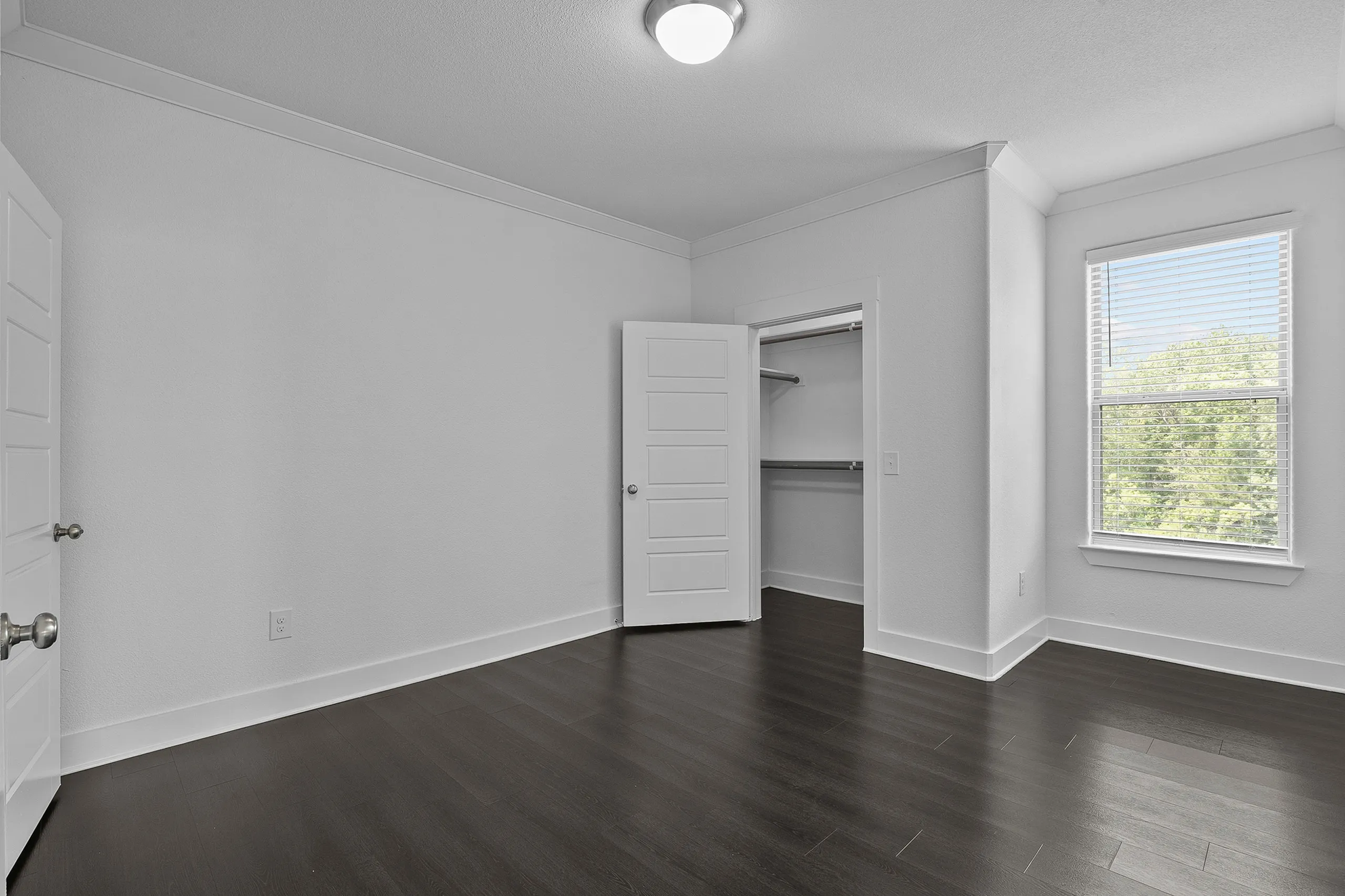 Bright, spacious bedroom with elegant dark hardwood flooring, large closet, and sunlit window.