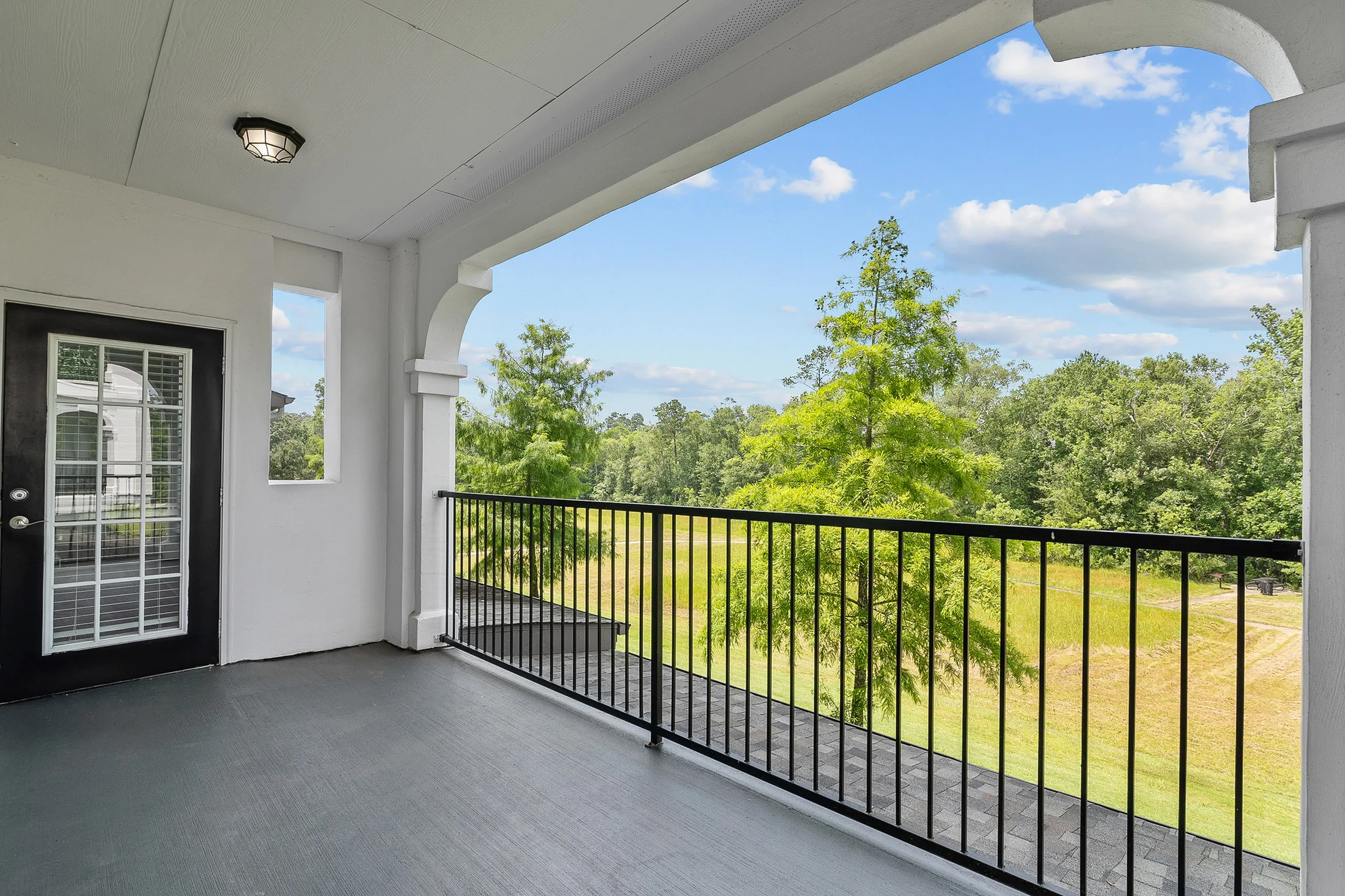 Charming balcony with elegant railing offering serene views of lush greenery and open skies.