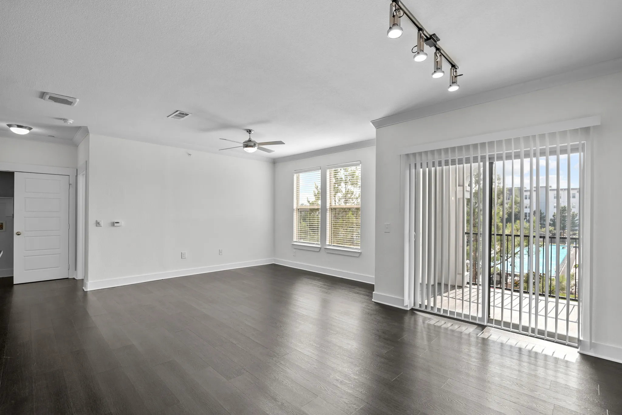 Bright and modern living room with sleek wooden floors, featuring large windows and a balcony view overlooking the pool.