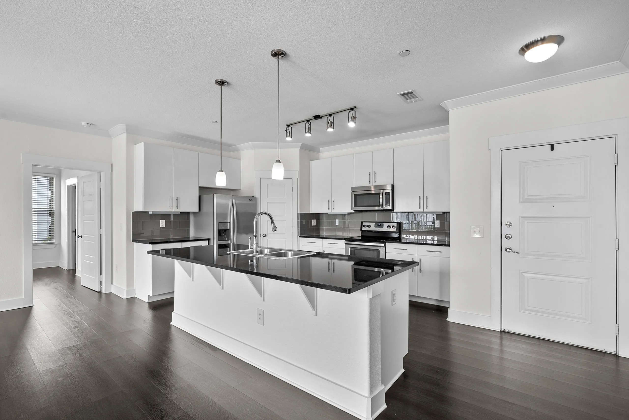 Modern kitchen with sleek black countertops, stainless steel appliances, and ample white cabinetry, accented by stylish pendant lighting.
