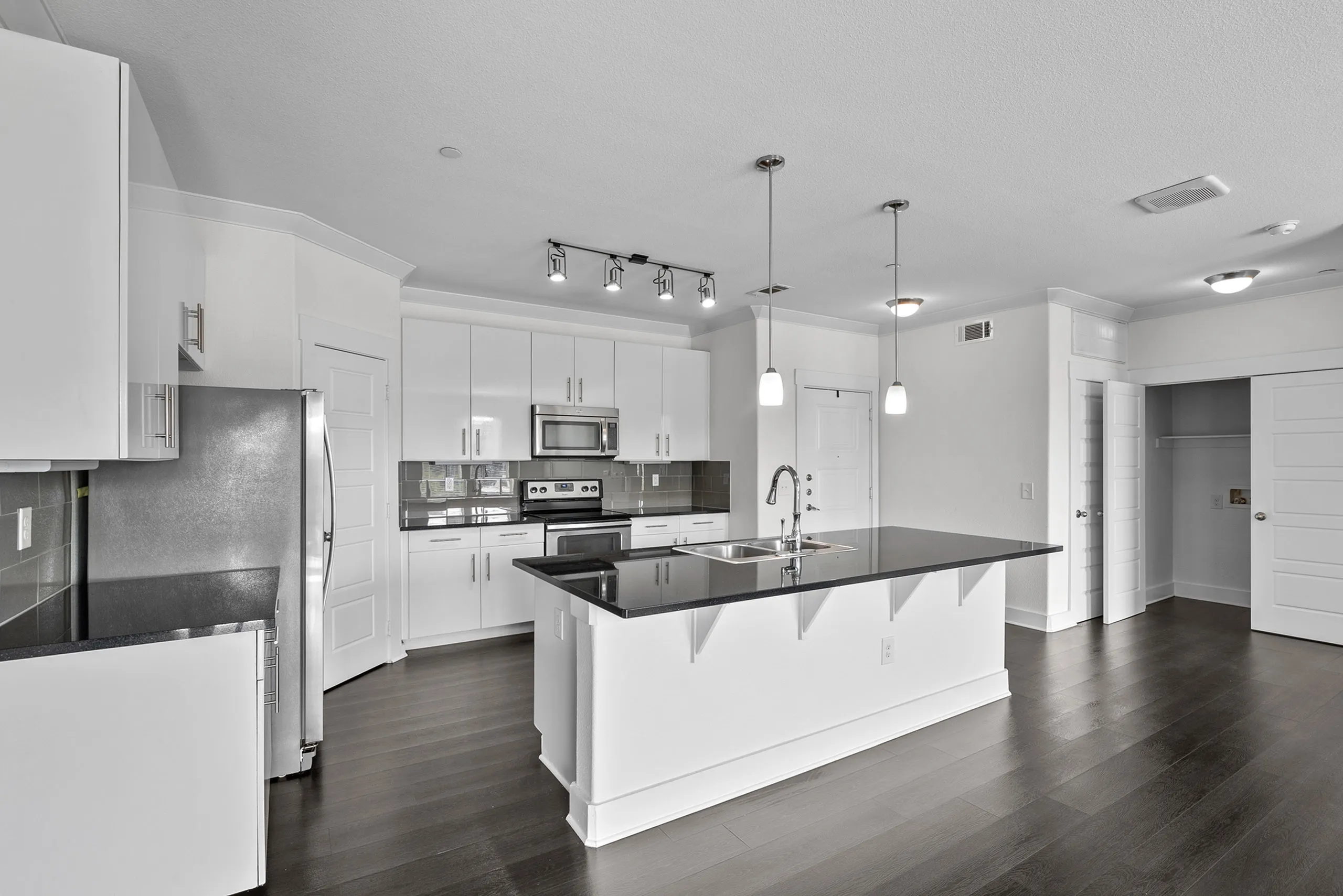 Sleek, modern kitchen with white cabinetry, stainless steel appliances, and elegant pendant lighting over a spacious island.