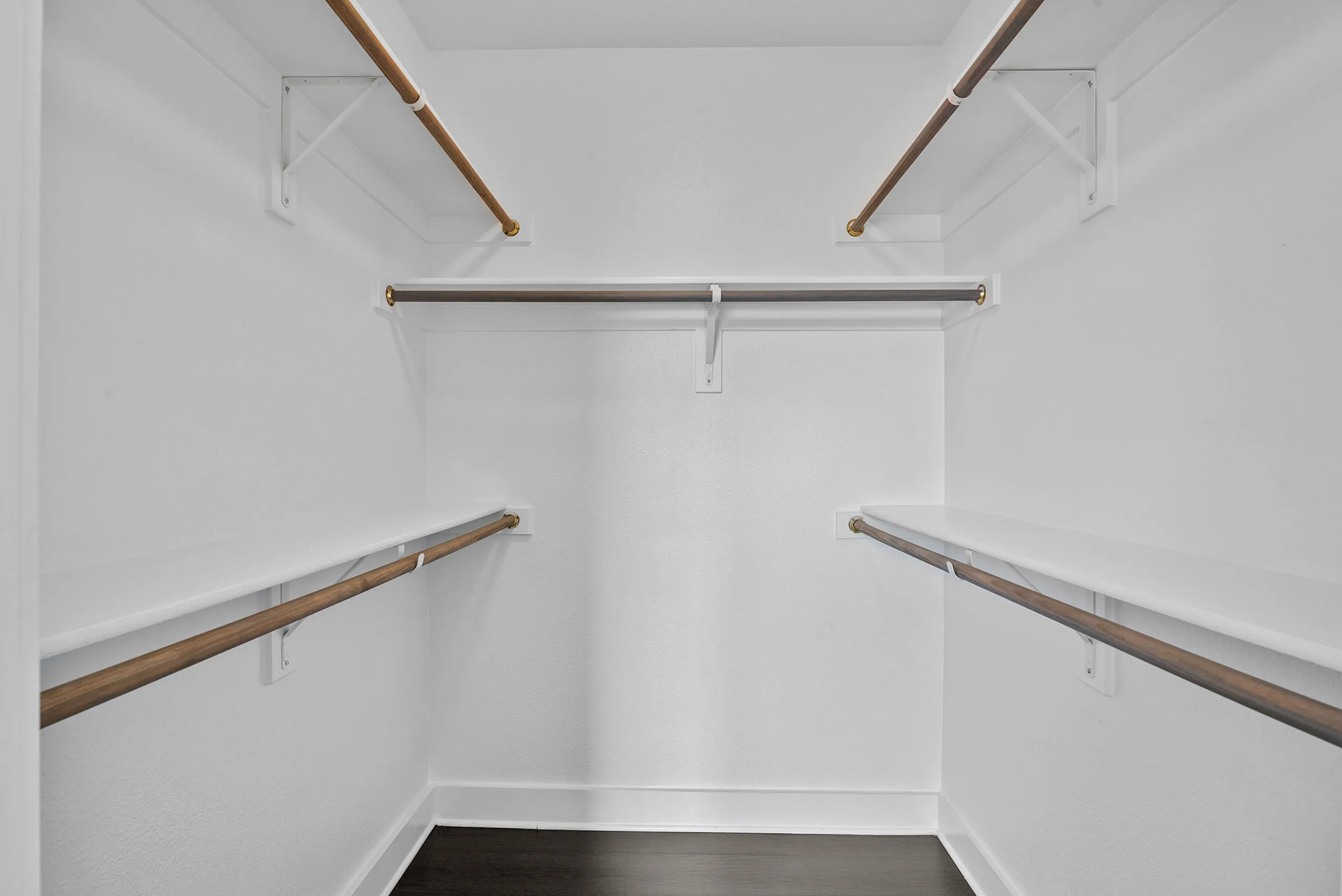 Spacious walk-in closet with multiple wooden hanging rods and bright white walls, offering ample storage space.