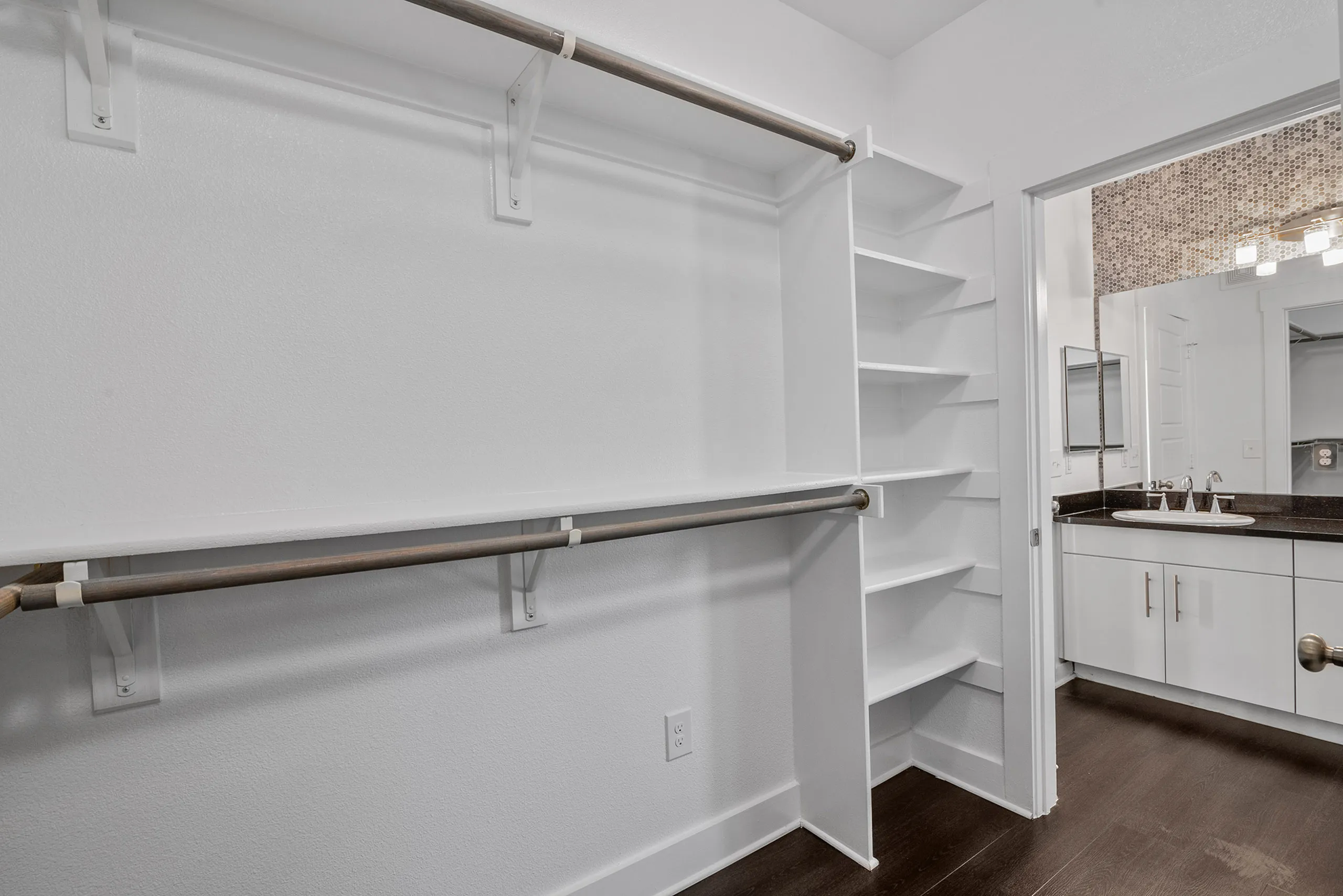 Elegant walk-in closet with ample shelving and hanging space, leading to a modern bathroom with dual sinks and stylish fixtures.