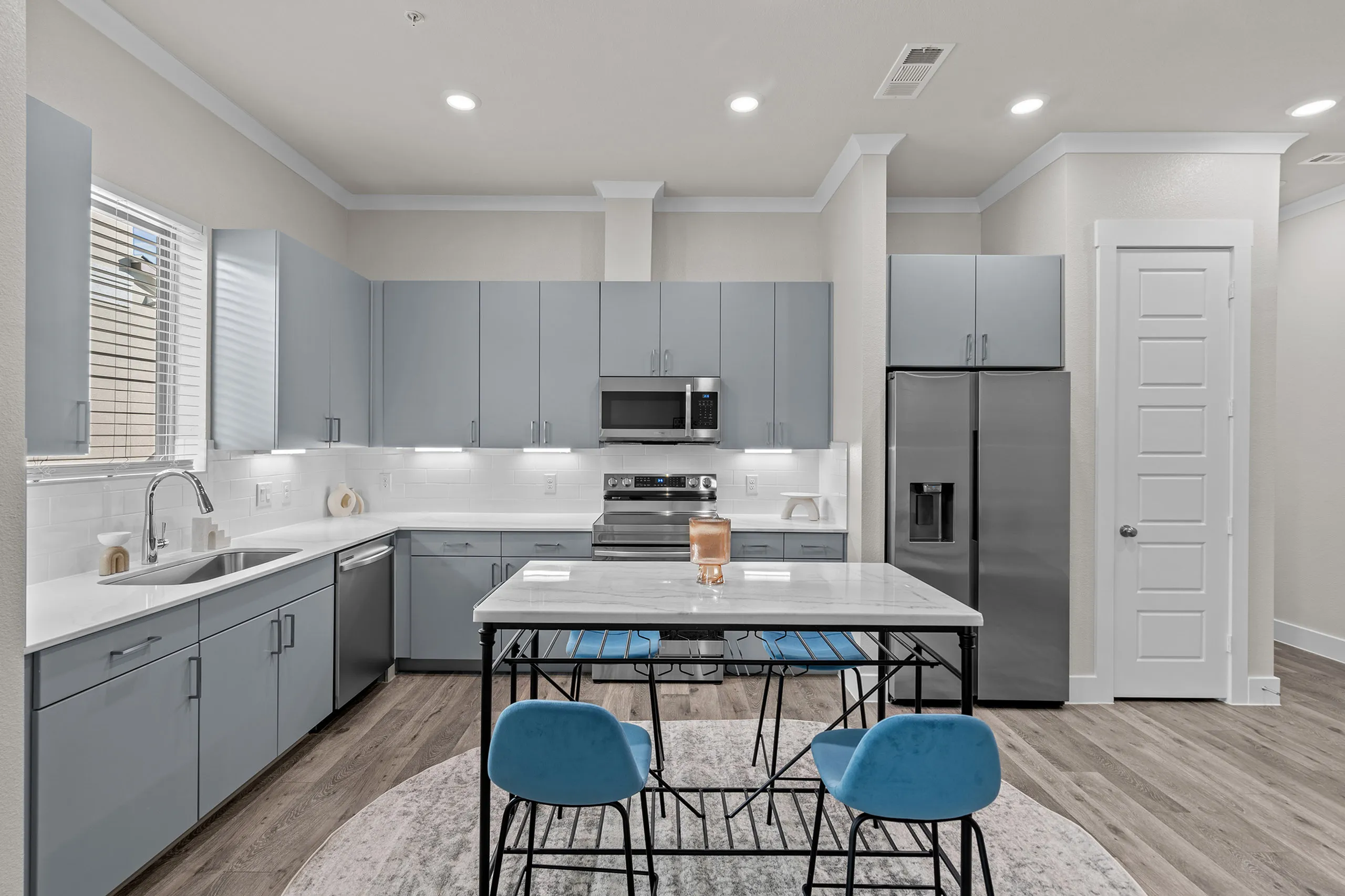 Modern kitchen with sleek gray cabinets, stainless steel appliances, and a chic island featuring blue chairs, perfect for contemporary living.