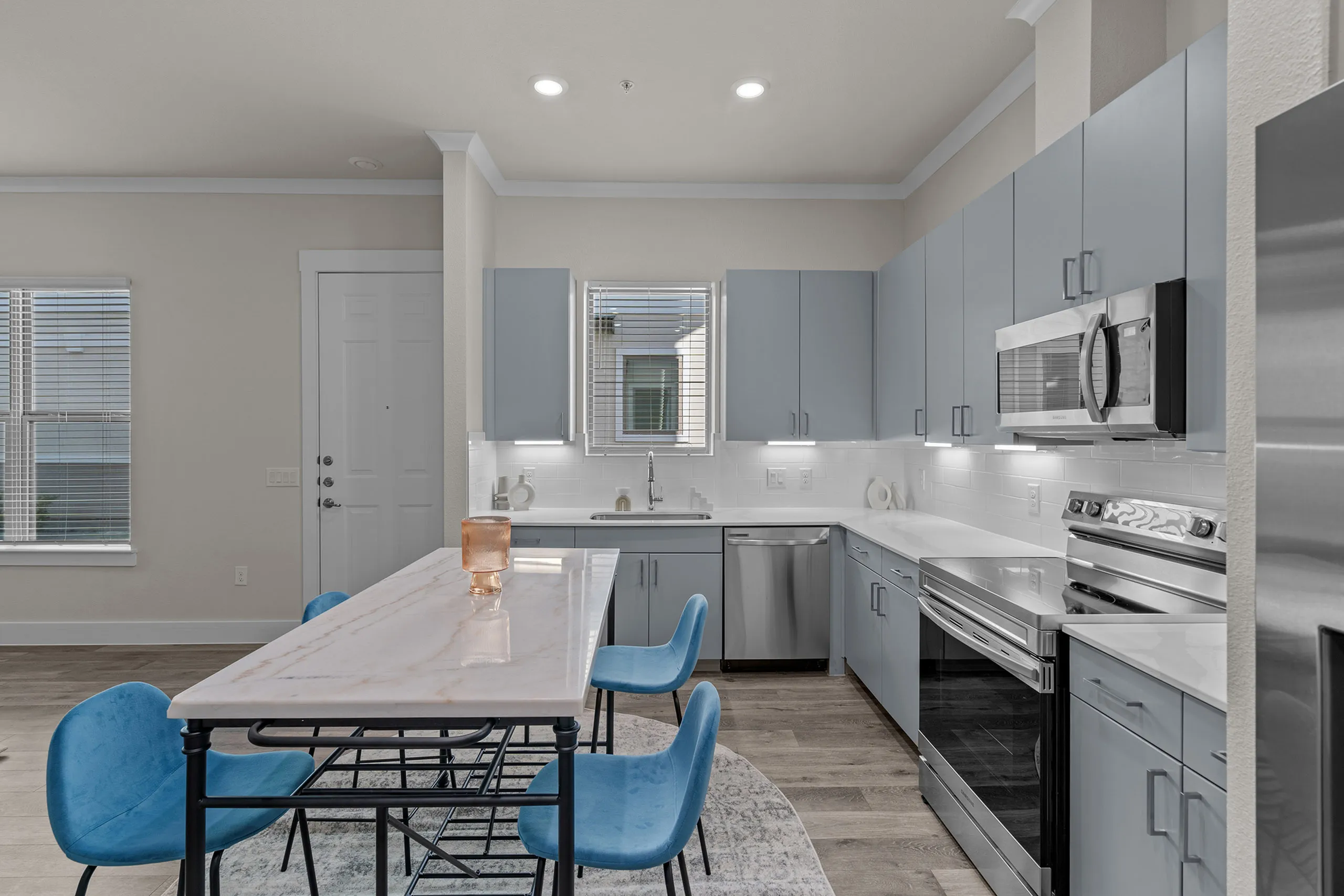 Modern kitchen with sleek grey cabinets, stainless steel appliances, and a stylish marble island with blue chairs.
