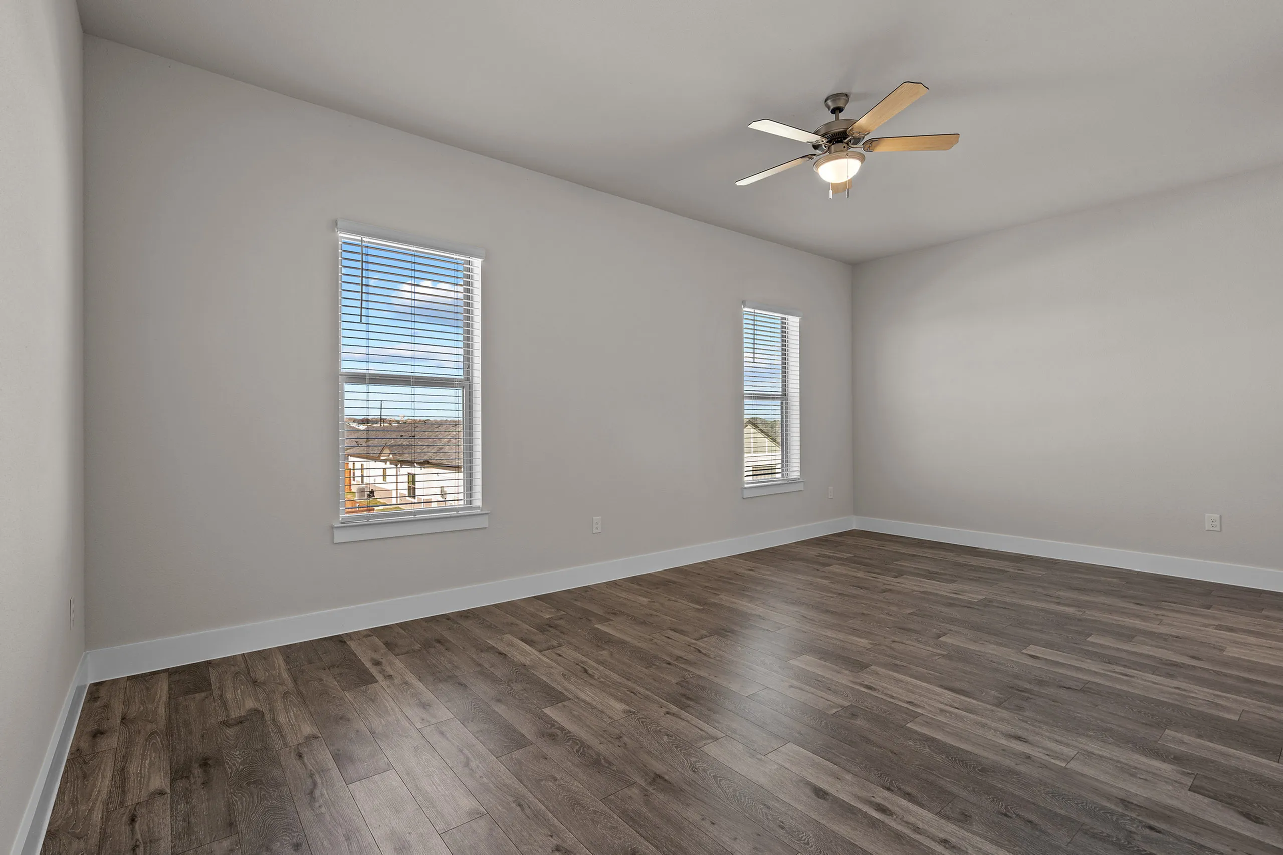 Bright and spacious room with elegant wood flooring, large windows offering a scenic view, and a stylish ceiling fan.