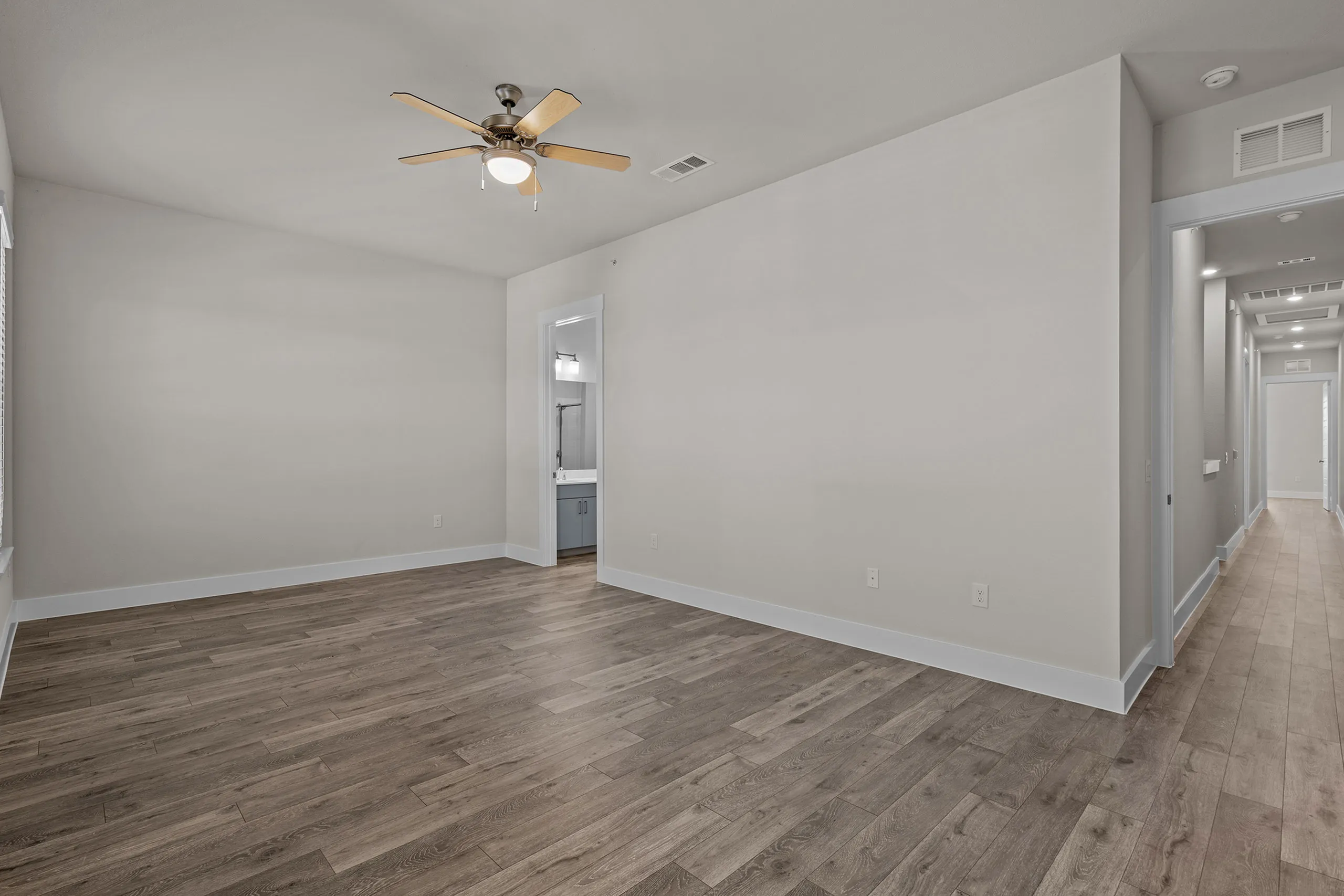 Spacious modern room with elegant hardwood flooring and ceiling fan, adjacent to a hallway and bathroom.