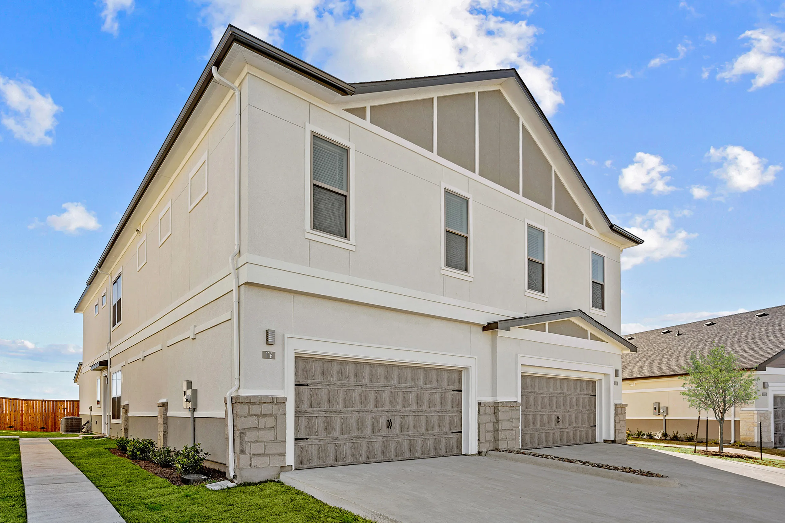 Modern two-story townhouse with dual garages, elegant exterior design, and lush green landscaping under a clear blue sky.