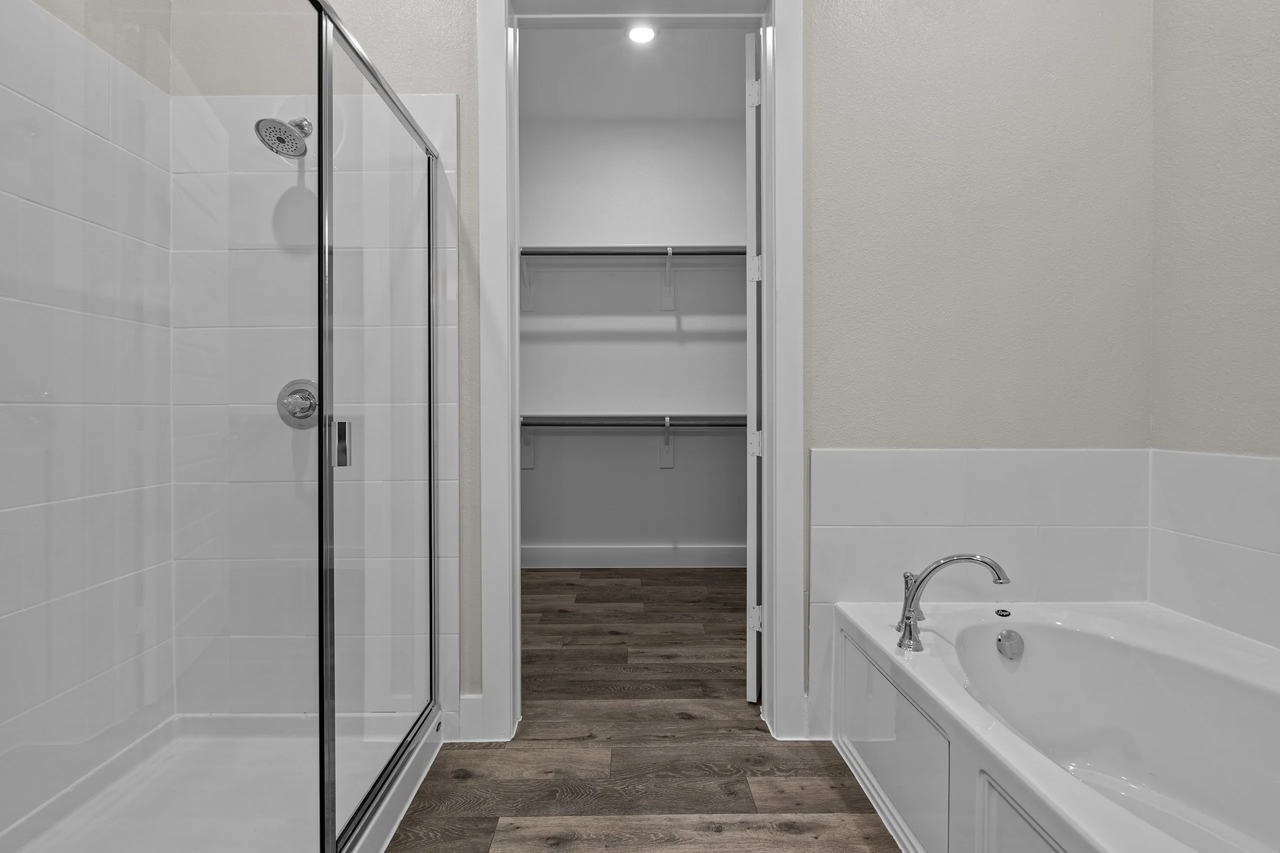 Modern bathroom featuring a sleek glass walk-in shower, luxurious bathtub, and a spacious walk-in closet with wooden flooring.
