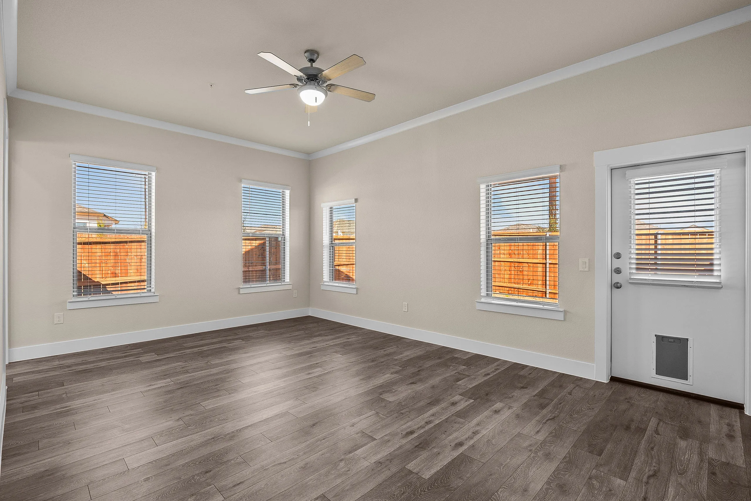 Bright and airy living room with elegant hardwood flooring, ceiling fan, and multiple windows offering natural light and outdoor views.