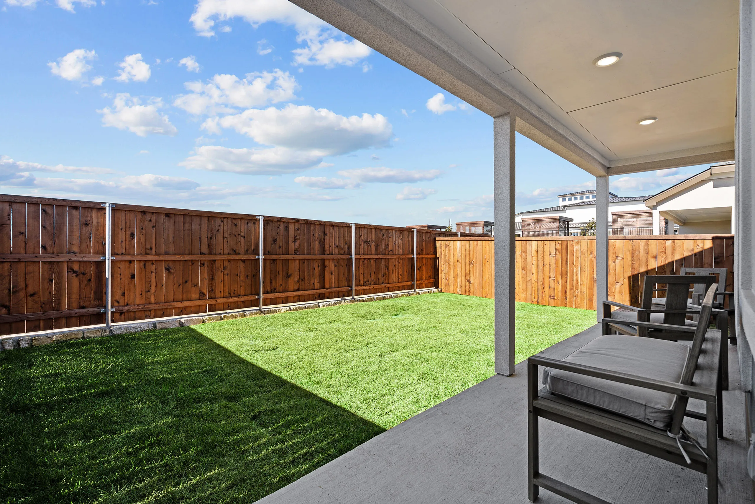 Charming backyard with lush green lawn, wooden fence, and cozy patio seating under a covered porch.